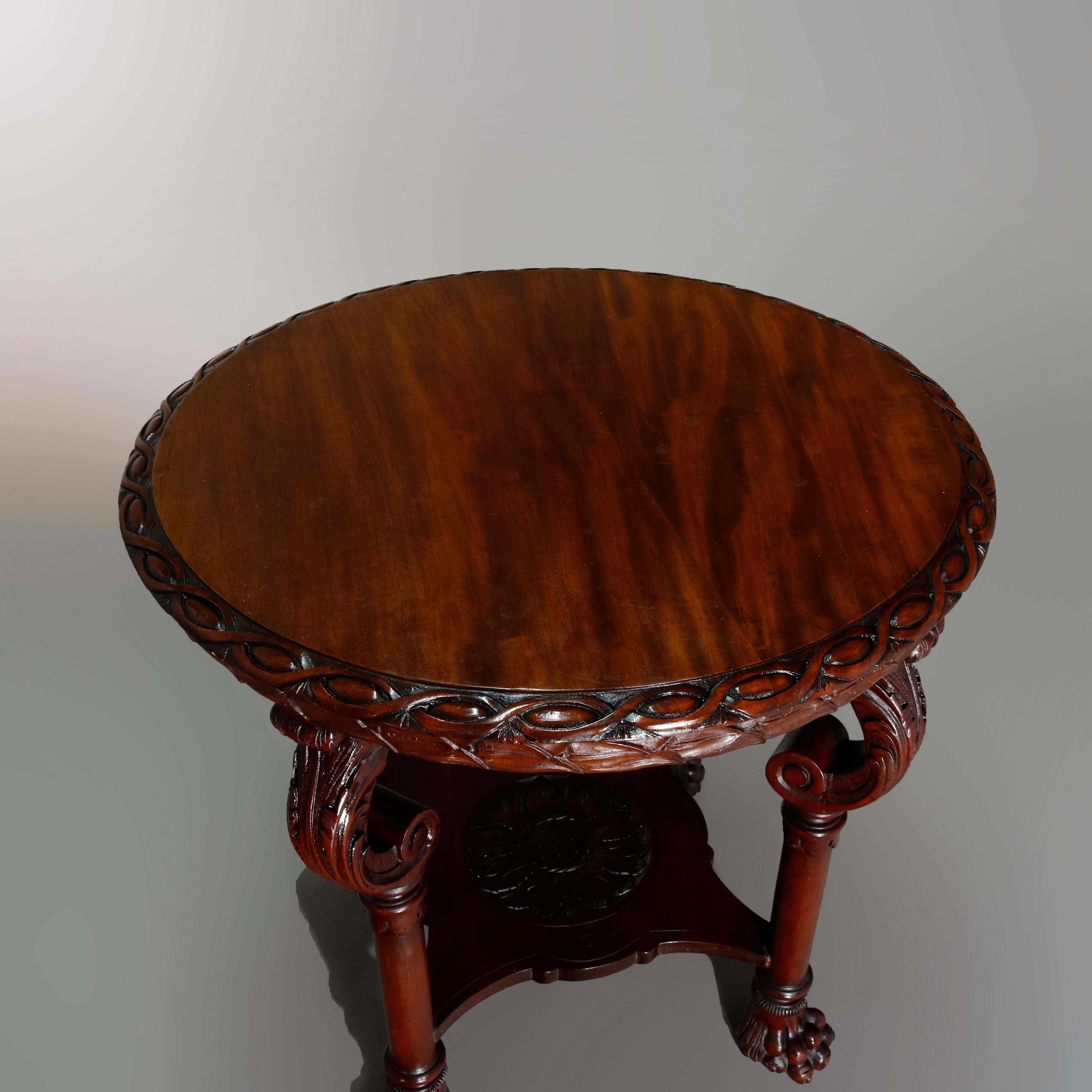 An antique American Empire center table offers mahogany construction with top having carved twist bordering surmounting quadruped base with column-form legs having carved scrolled acanthus capitals, lower display shelf and paw feet, circa