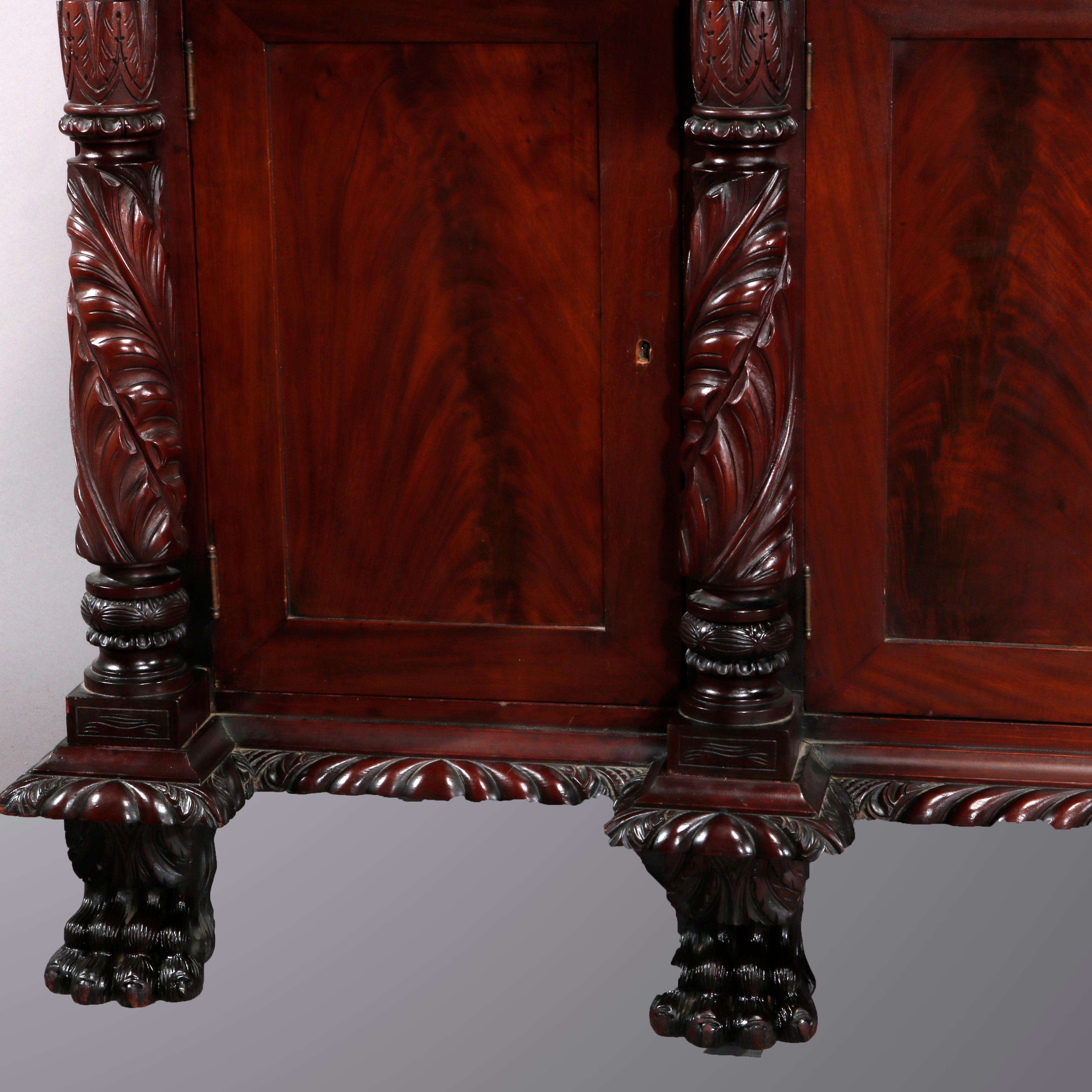 An antique American Empire sideboard offers flame mahogany construction with top having backsplash and rope twist bordering, surmounting case with three bow front drawers over four door cabinet with flanking deeply carved foliate columns, raised on