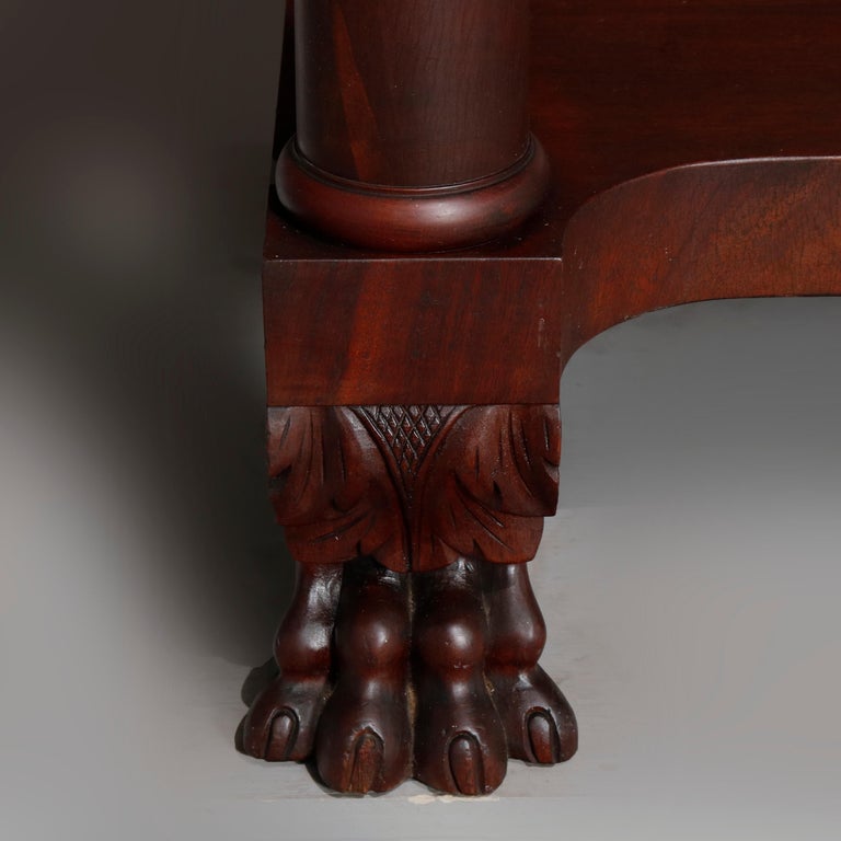 An antique American Empire classical server offers deeply striated flame mahogany construction with case having convex frieze drawer with glass pulls and raised on Corinthian column supports resting on lower shelf and having cared paw feet, circa