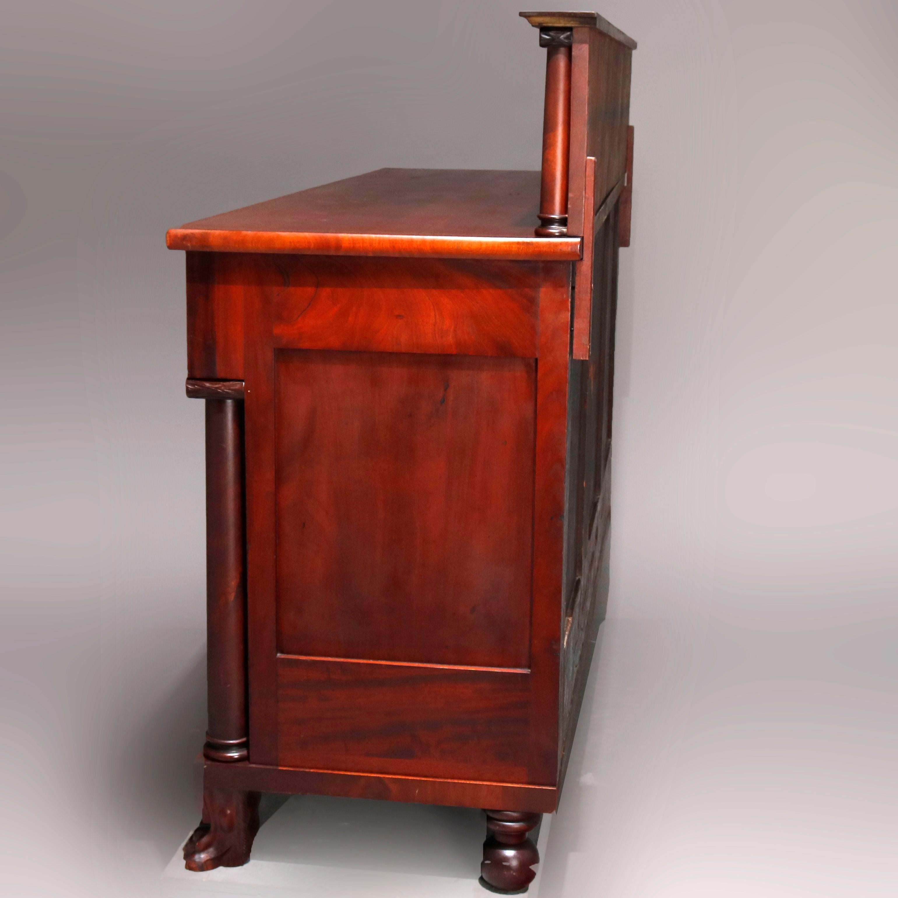 An antique American Empire Classical sideboard offers flame mahogany construction with oversized backsplash with carved Corinthian columns over counter surmounting case with upper drawers over central convex cabinet flanked by side compartments and