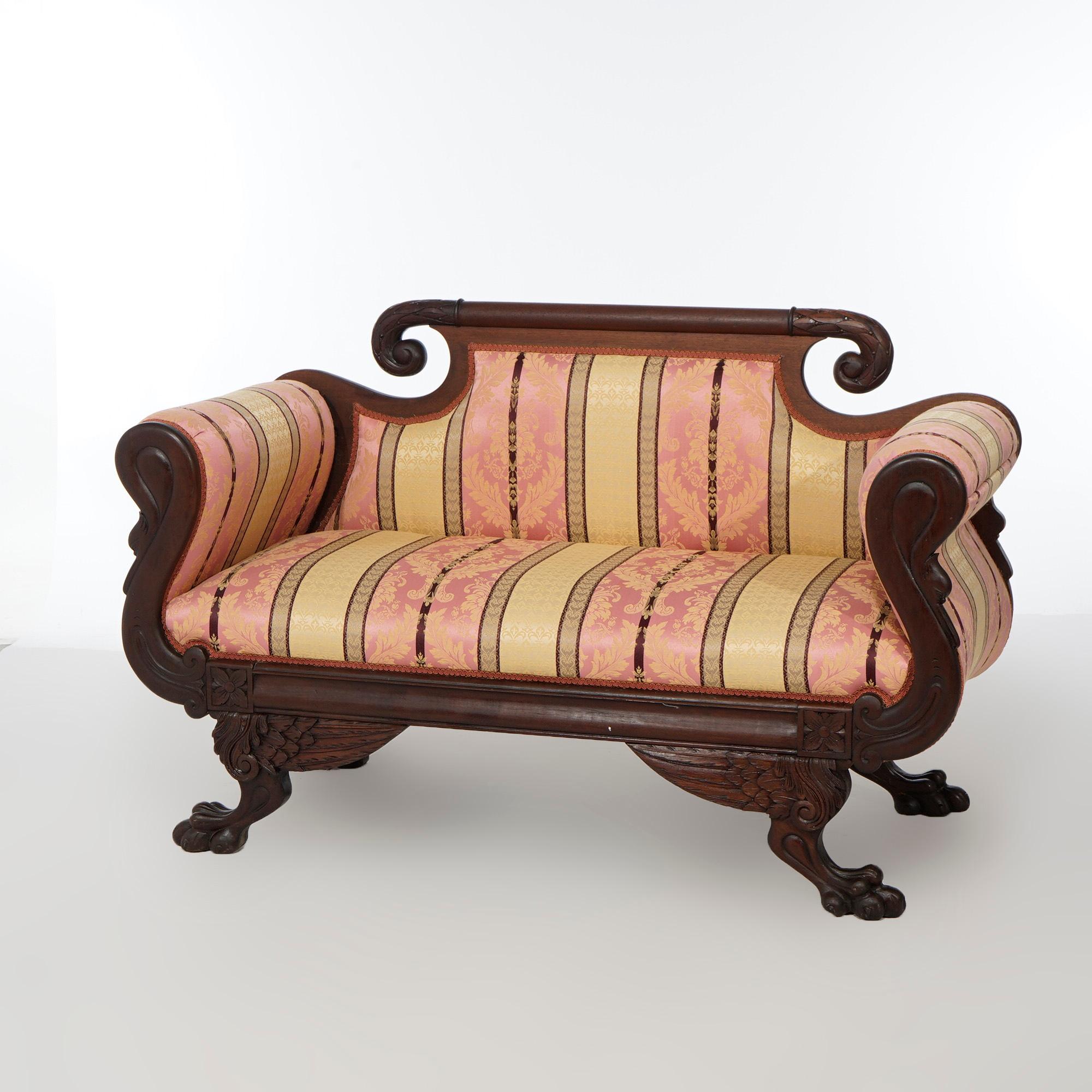 An antique American Empire Classical Greco figural sofa offers mahogany frame with scroll form crest over upholstered back, seat and arms, carved gooseneck arms, raised on foliate carved legs terminating in paw feet, c1840.
***Matching armchair