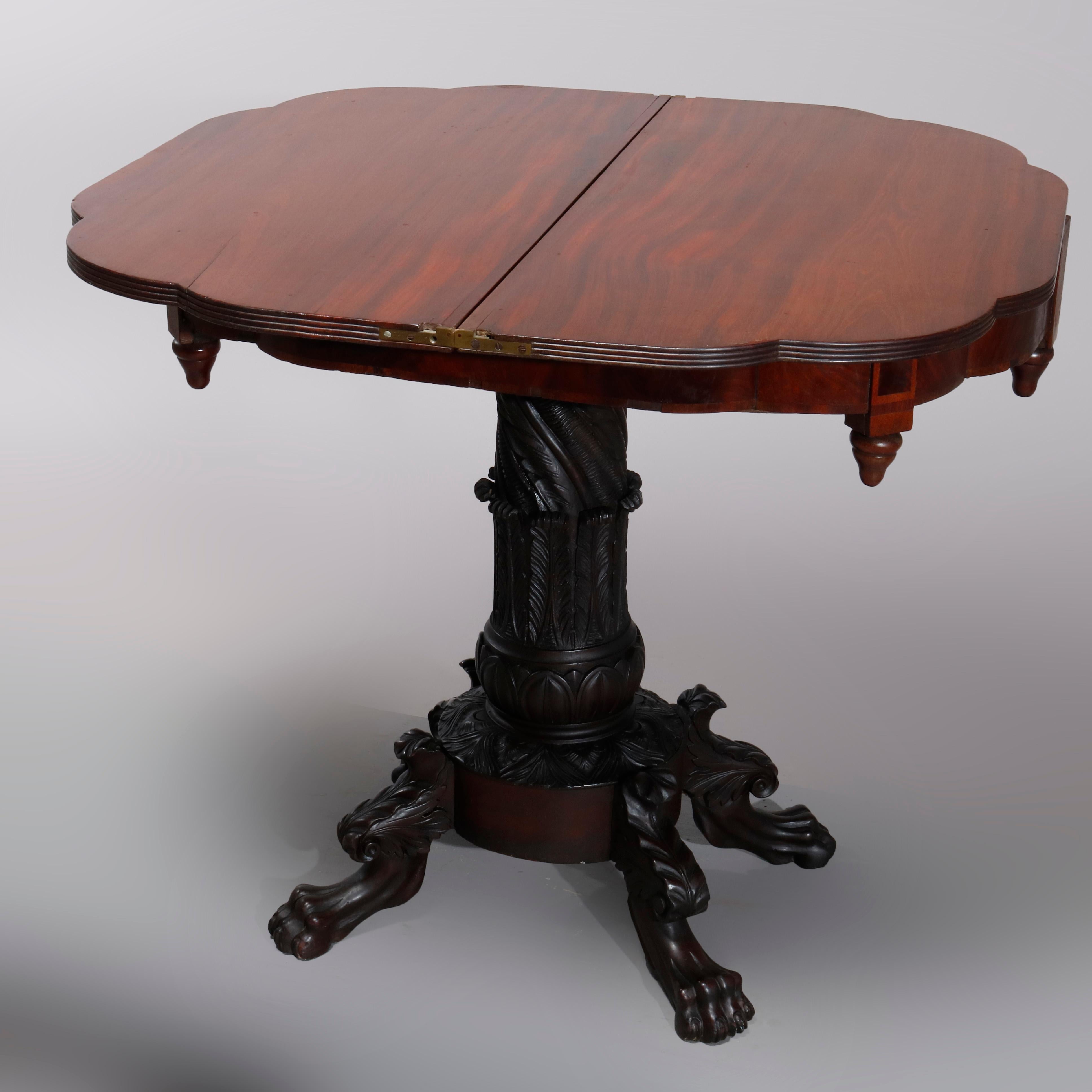 An antique American Empire game table offers flame mahogany construction with shaped demilune top having deep skirt with drop finials and surmounting heavily carved acanthus foliate pedestal base raised on carved legs terminating in paw feet, circa