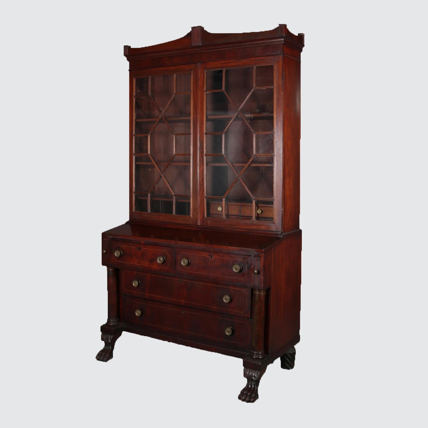 An American Empire flame mahogany secretary features upper bookcase with double fretwork glass doors opening to adjustable shelf interior with drawers and pigeon holes surmounting case having drop front writing above two frieze drawers over two long