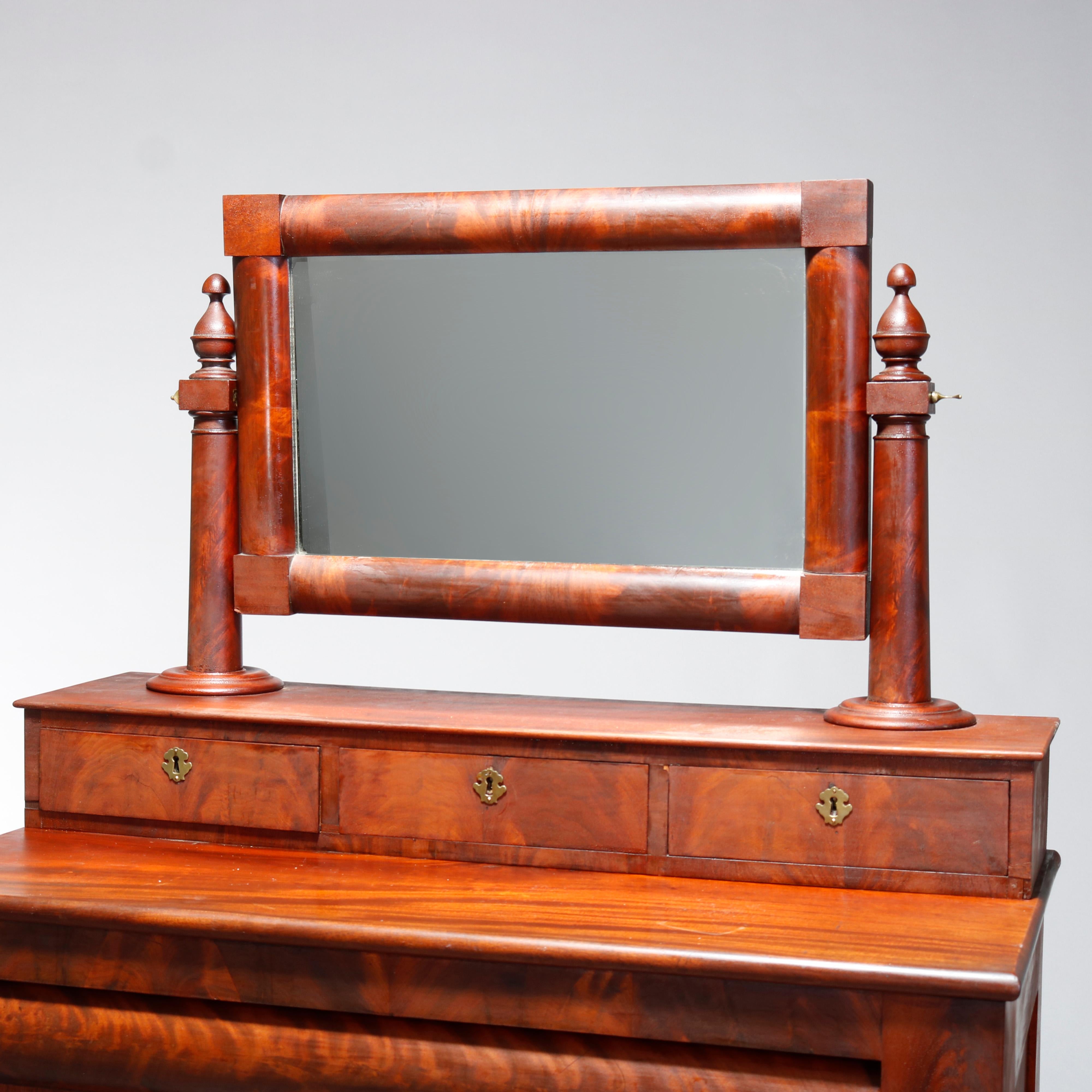 An antique American Empire high chest offers paneled flame mahogany construction with upper swivel mirror having flanking column supports with finals and surmounting case with glove boxes over convex frieze drawer and three long drawers flanked by