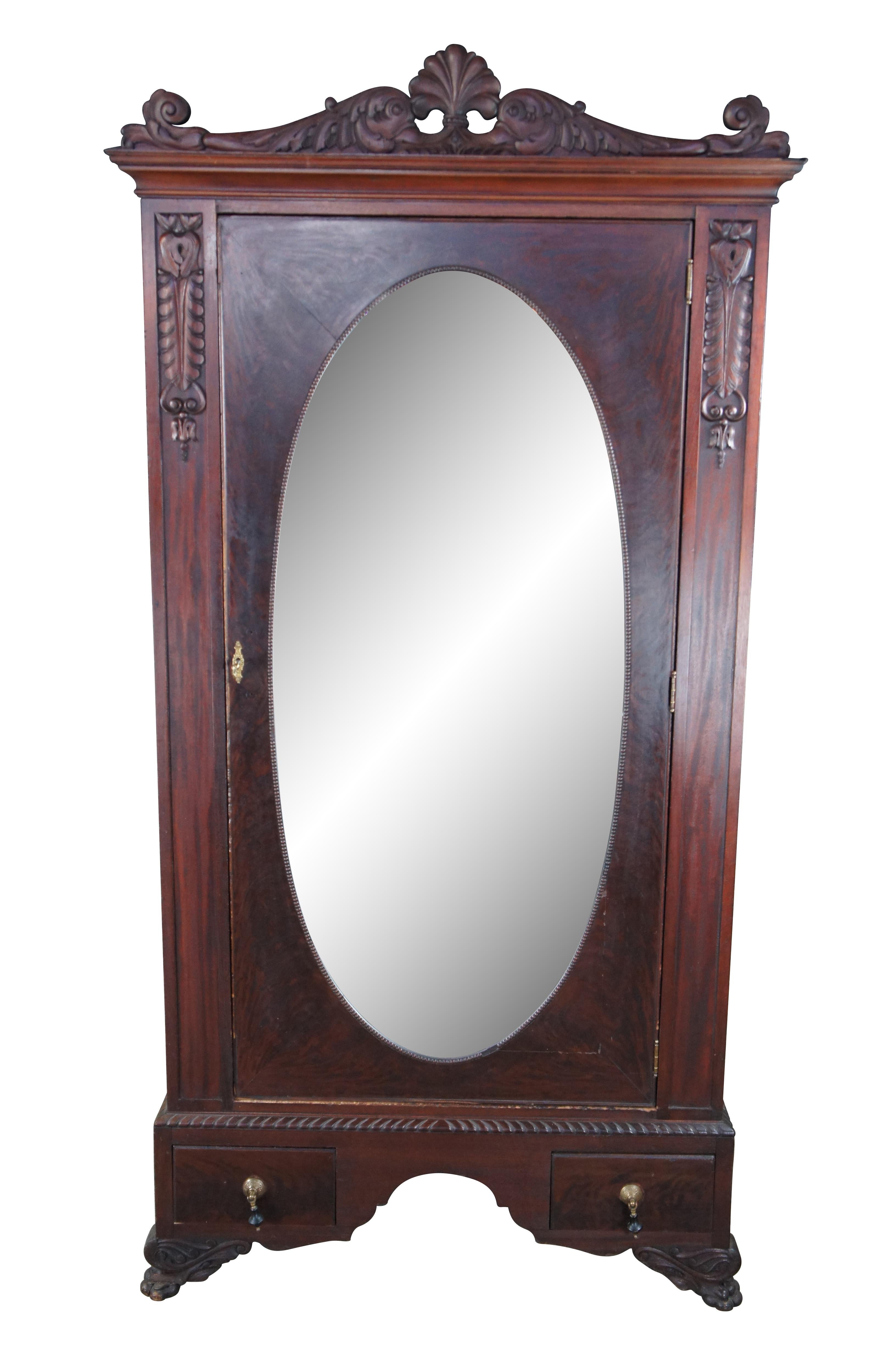 An exceptional early 20th century armoire.  Features a rectangular frame made from mahogany with figural and acanthus carved accents.  The central door features a large oval mirror that opens to space for hanging garments.  The base features an