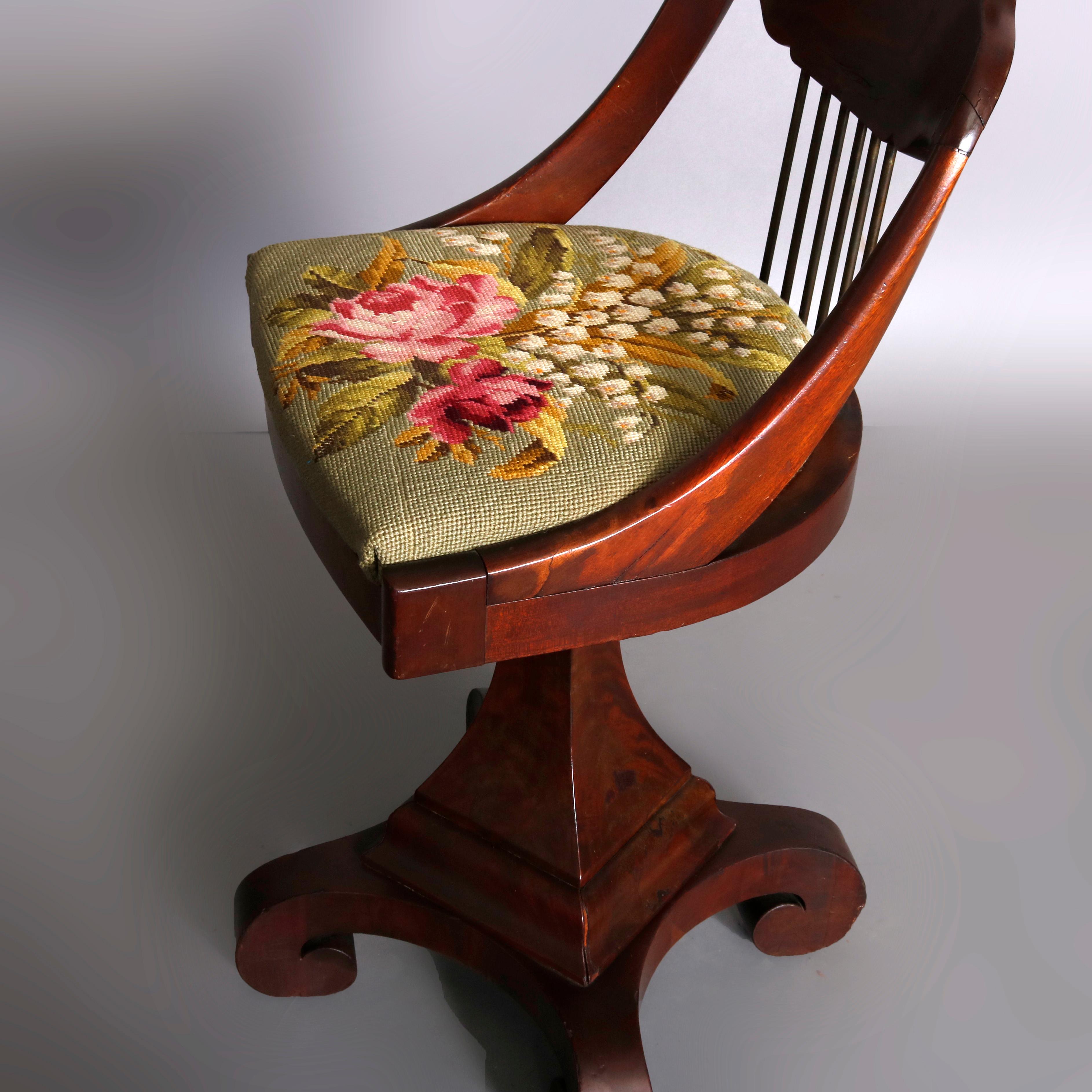 A classical American Empire piano chair offers flame mahogany construction with shaped spindle back over floral needlepoint upholstered seat surmounting flared and faceted column raised on scroll form feet, circa 1840

***DELIVERY NOTICE – Due to