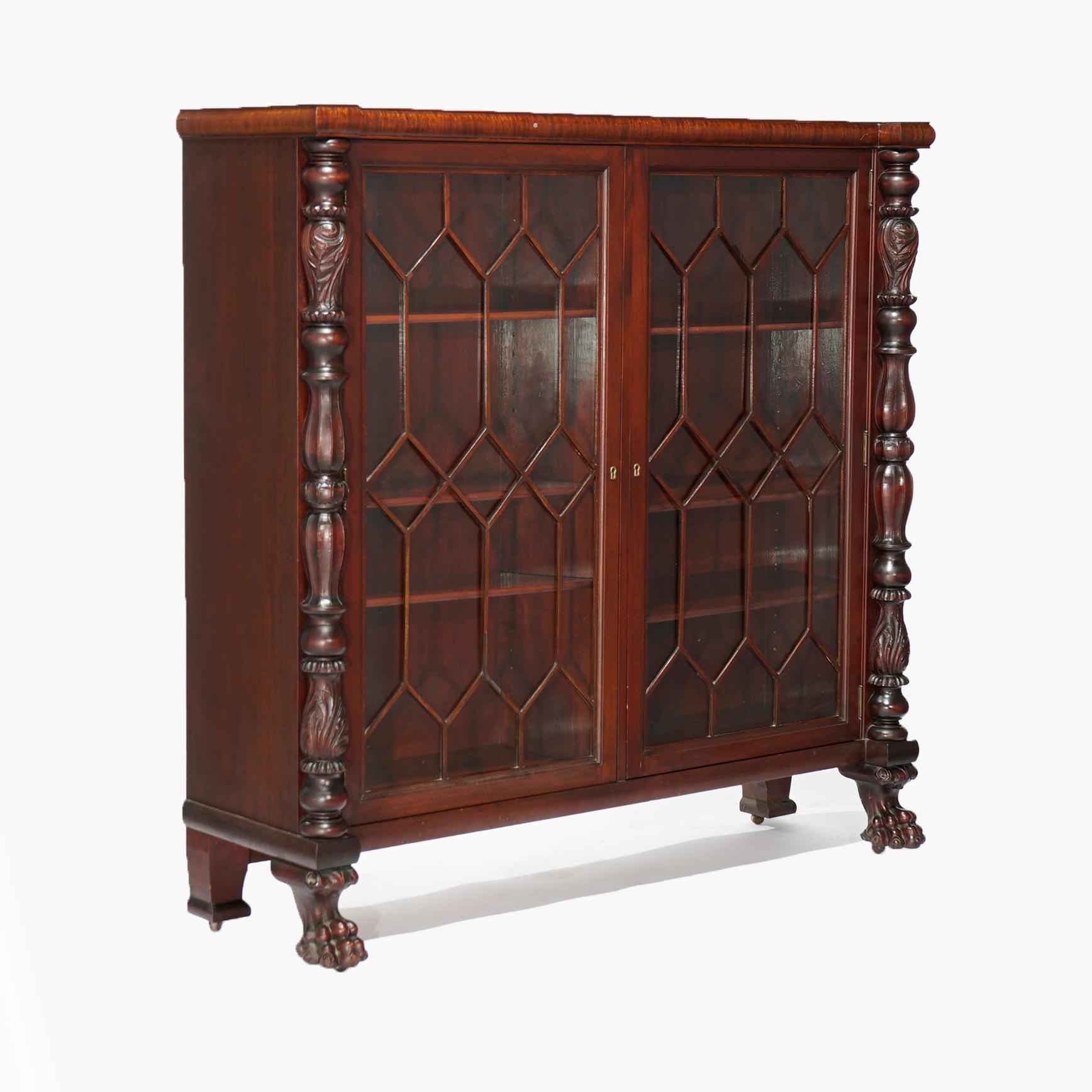 An antique American Empire enclosed bookcase offers flame mahogany construction in Neoclassical form with two glass doors with mullioned overlay opening to divided and adjustable shelf interior, flanked by balustrade columns with carved foliate
