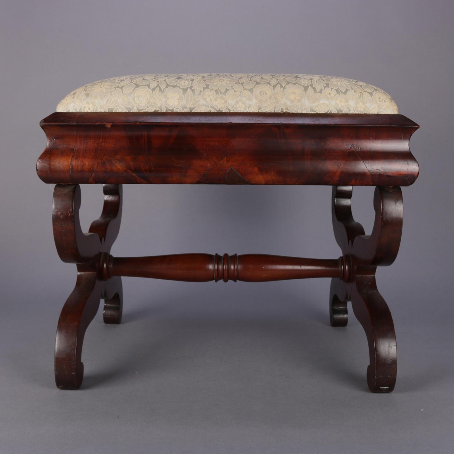 An antique flame mahogany American Empire footstool featuring upholstered cushion seated in ogee frame over s-scroll trestle base with turned stretcher, circa 1840

Measures: 16.75