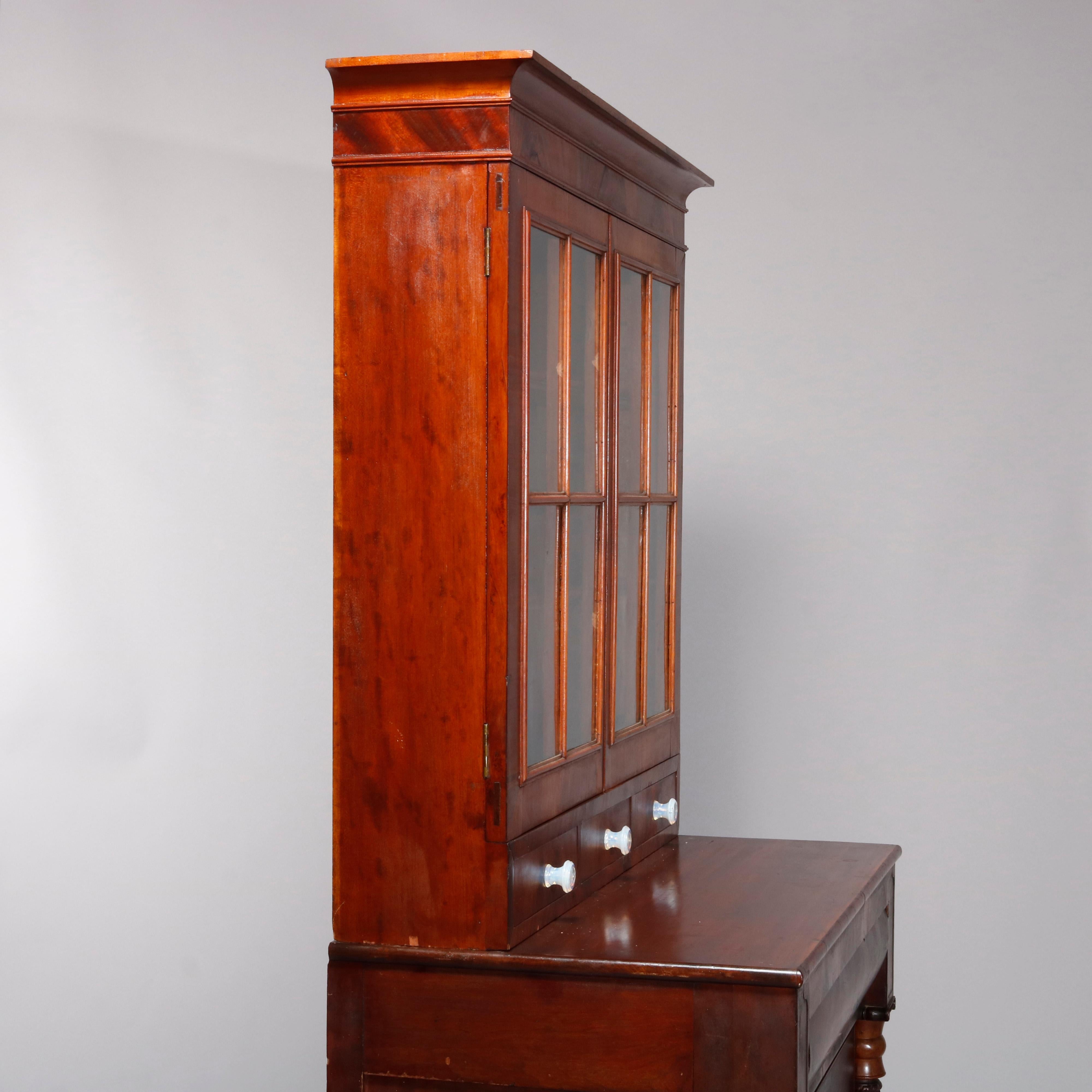An antique American Empire book or display case over chest of drawers in the manner of Anthony Quervelle offers flame mahogany construction with upper bookcase having double glass doors and three drawers surmounting lower case with drawers flanked