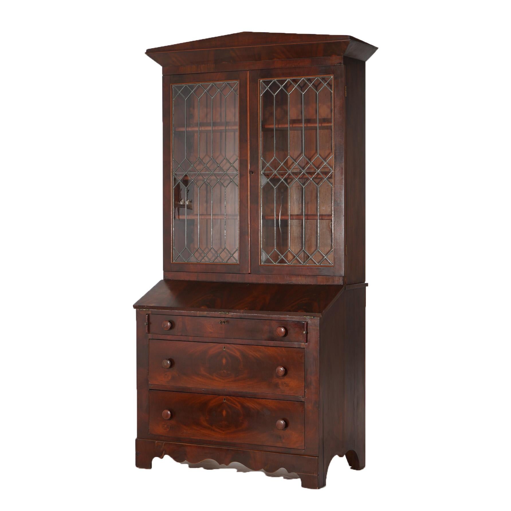 An antique American Empire secretary offers flame mahogany construction with upper having arched pediment over bookcase having double doors with leaded glass over lower with slant front desk and long drawers, c1840

Measures - 87