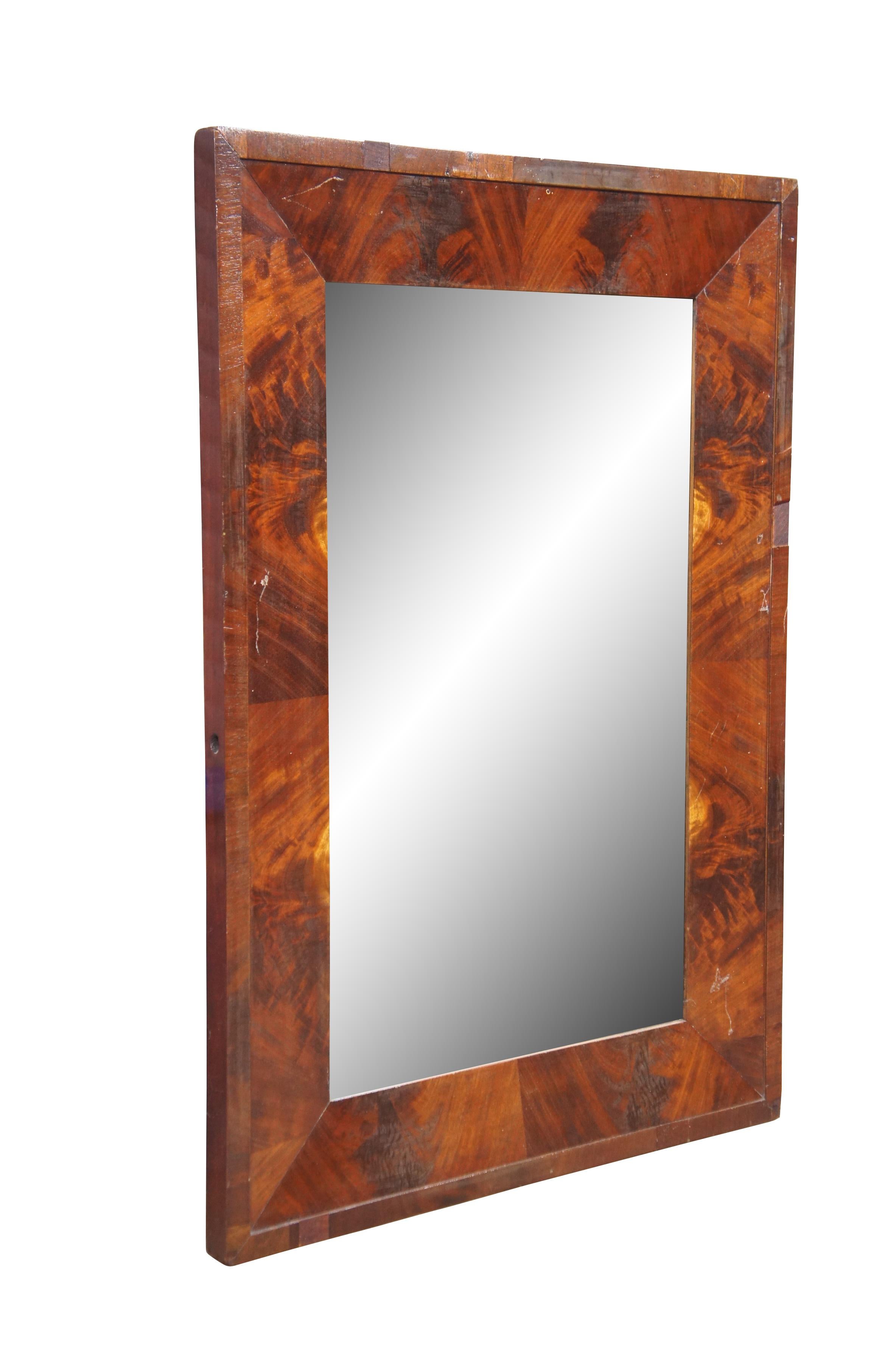 Miroir mural rectangulaire ancien de style Empire américain avec un cadre biseauté en acajou flammé. Les trous sur les côtés indiquent que le miroir faisait autrefois partie d'un support de rasage ou d'une coiffeuse.

Dimensions :
17,75