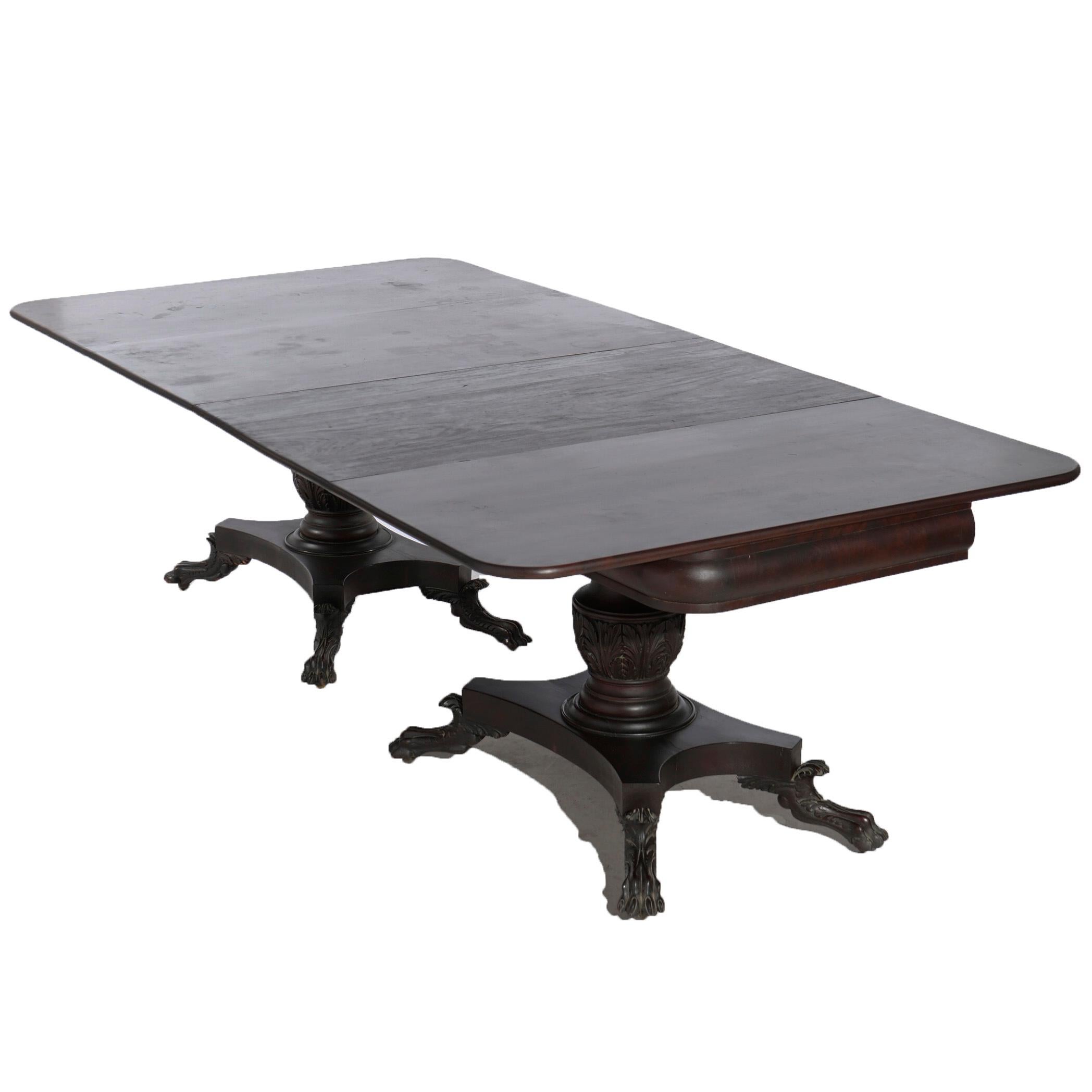 An antique American Empire Greco banquet dining table offers flame mahogany construction in Neoclassical form with drop leaf dining top over carved urn form double pedestals and raised on bases with carved paw feet, c1840

Measures- Overall 100.5''H