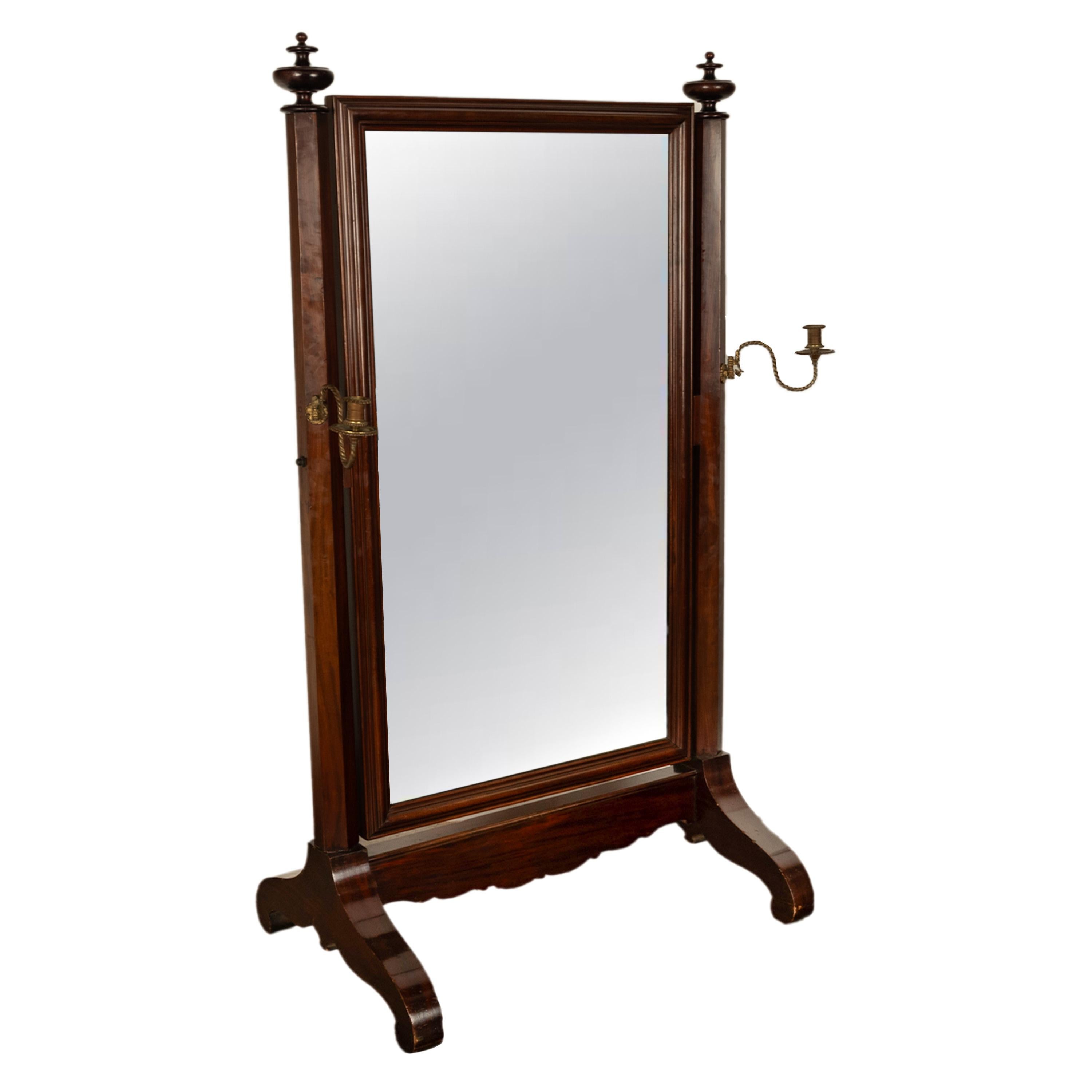 A good antique American Empire period mahogany freestanding cheval mirror, New York, circa 1830.
The mirror having twin large urn shaped turned finials to the top of a pair of octagonal columns, the columns are fitted with removable brass candle