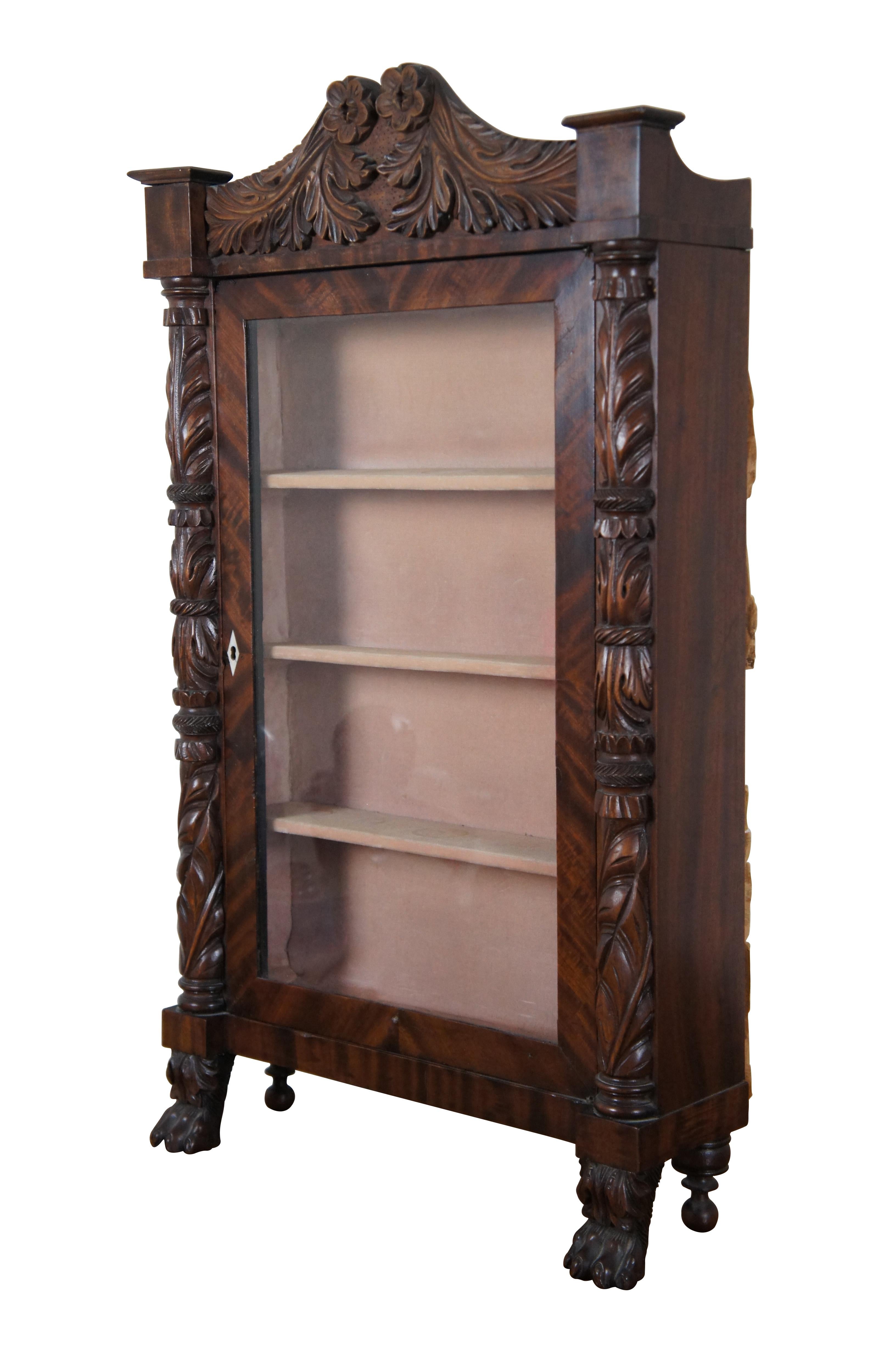 Antique American Empire carved mahogany glass front display cabinet / vitrine, heavily carved with spindle and paw / claw feet supporting foliate pillars that lead to a scrolled floral pediment. The glass door features a white diamond shaped inlaid