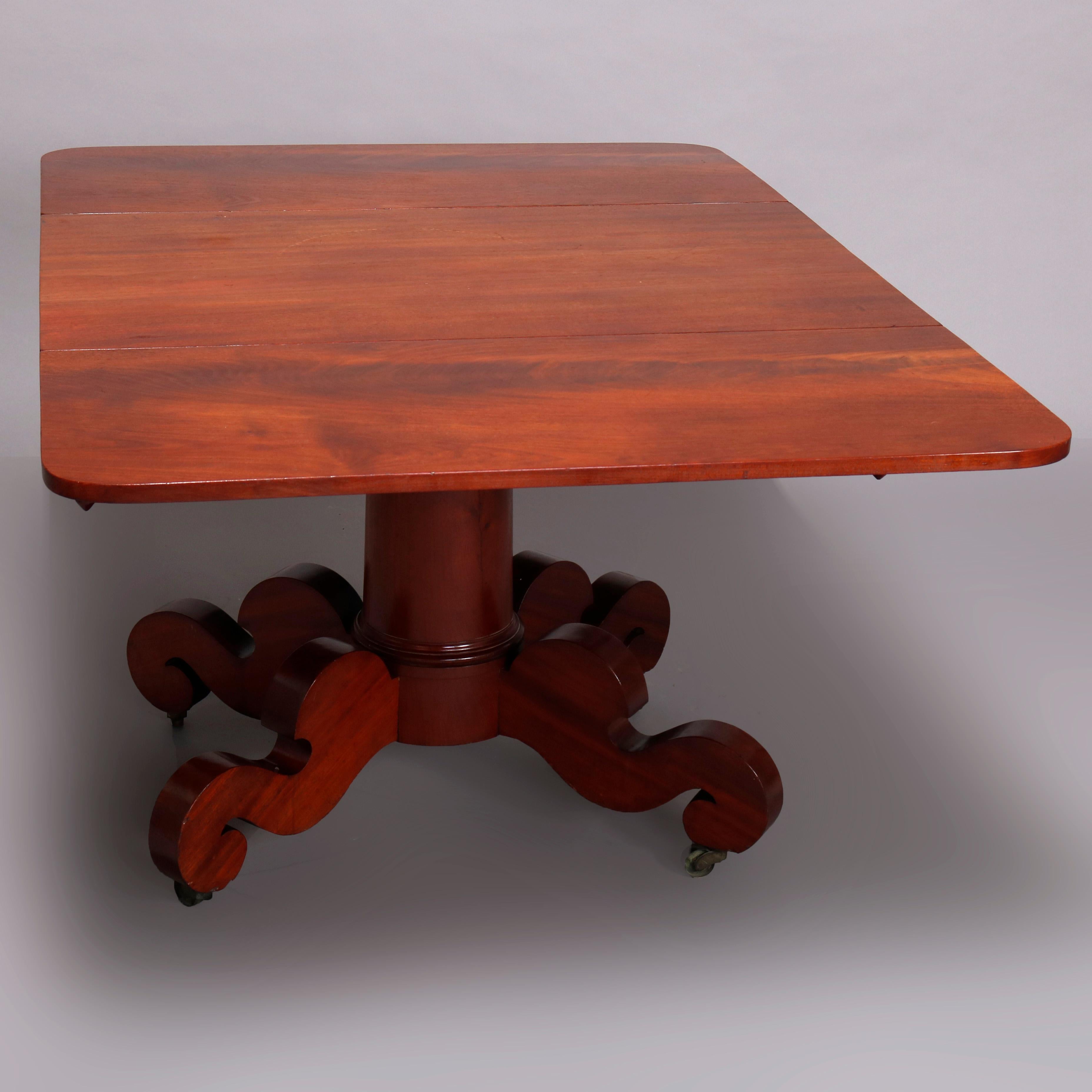 An antique American 
empire table in the manner of Joseph Meeks offers mahogany construction with top having drop leaves and raised on pedestal base with scroll form feet, c1840

Measures- 39