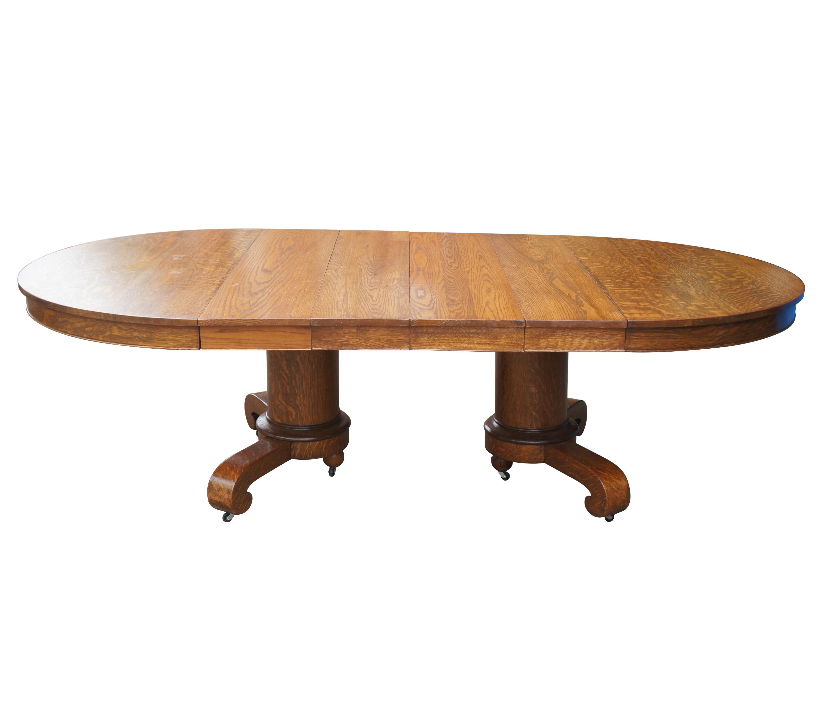 Late 19th century American Empire / Mission double pedestal dining table.  Made from Quartersawn Oak.  Features an extendable oval top over thick cylindrical pedestal bases with scrolled feet.  Includes 4 leaves for extension.  Table is on casters