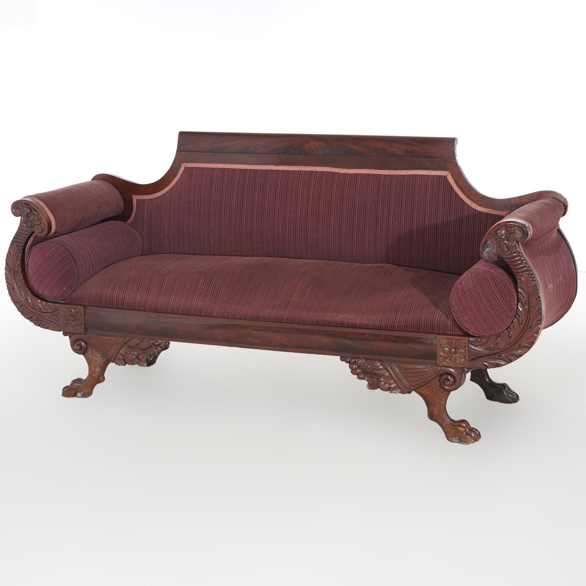 An antique Greco American Empire sofa offers upholstered flame mahogany construction in Neoclassical form having scroll form crest and arms, raised on carved paw feet, c1840

Measures  - 37.25