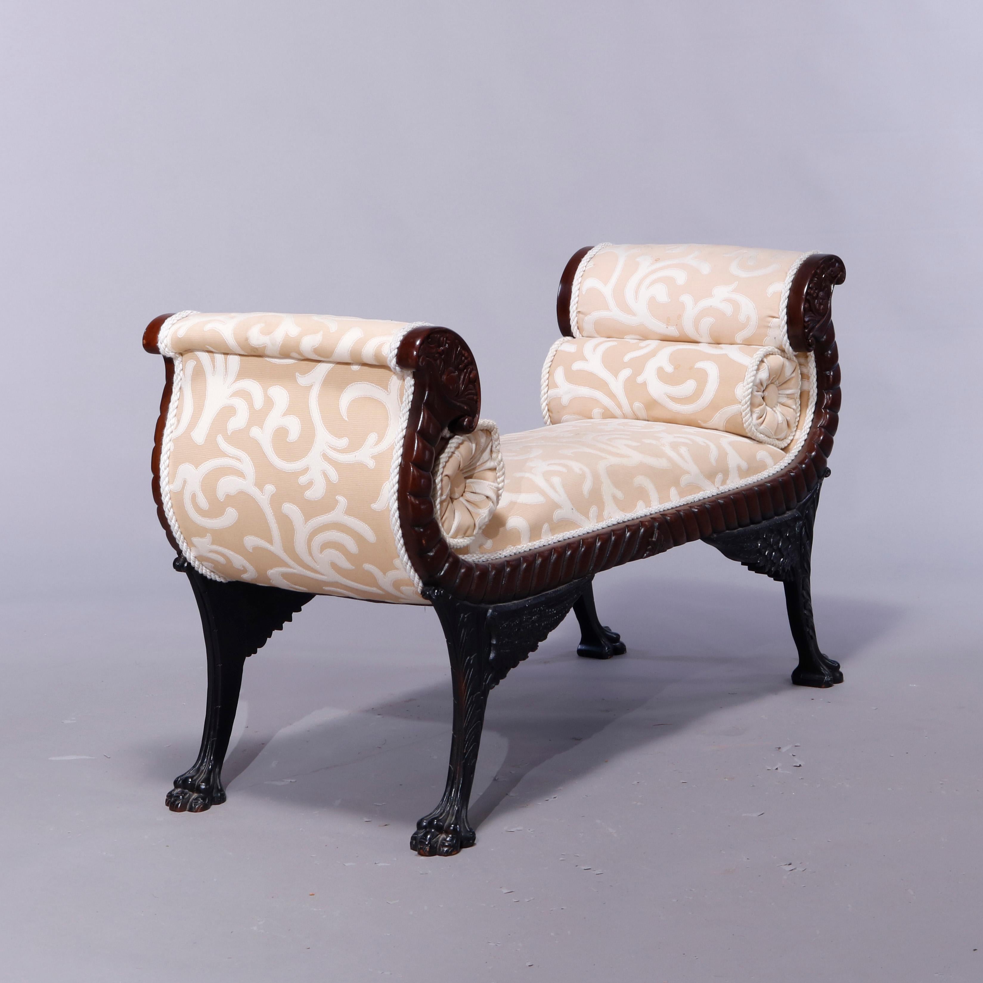 An antique American Empire neoclassical style upholstered window bench offers mahogany frame with carved scroll cornucopia form arms, rope twist frame, and raised on carved winged legs terminating in claw feet, 20th century 

Measures: 27.75