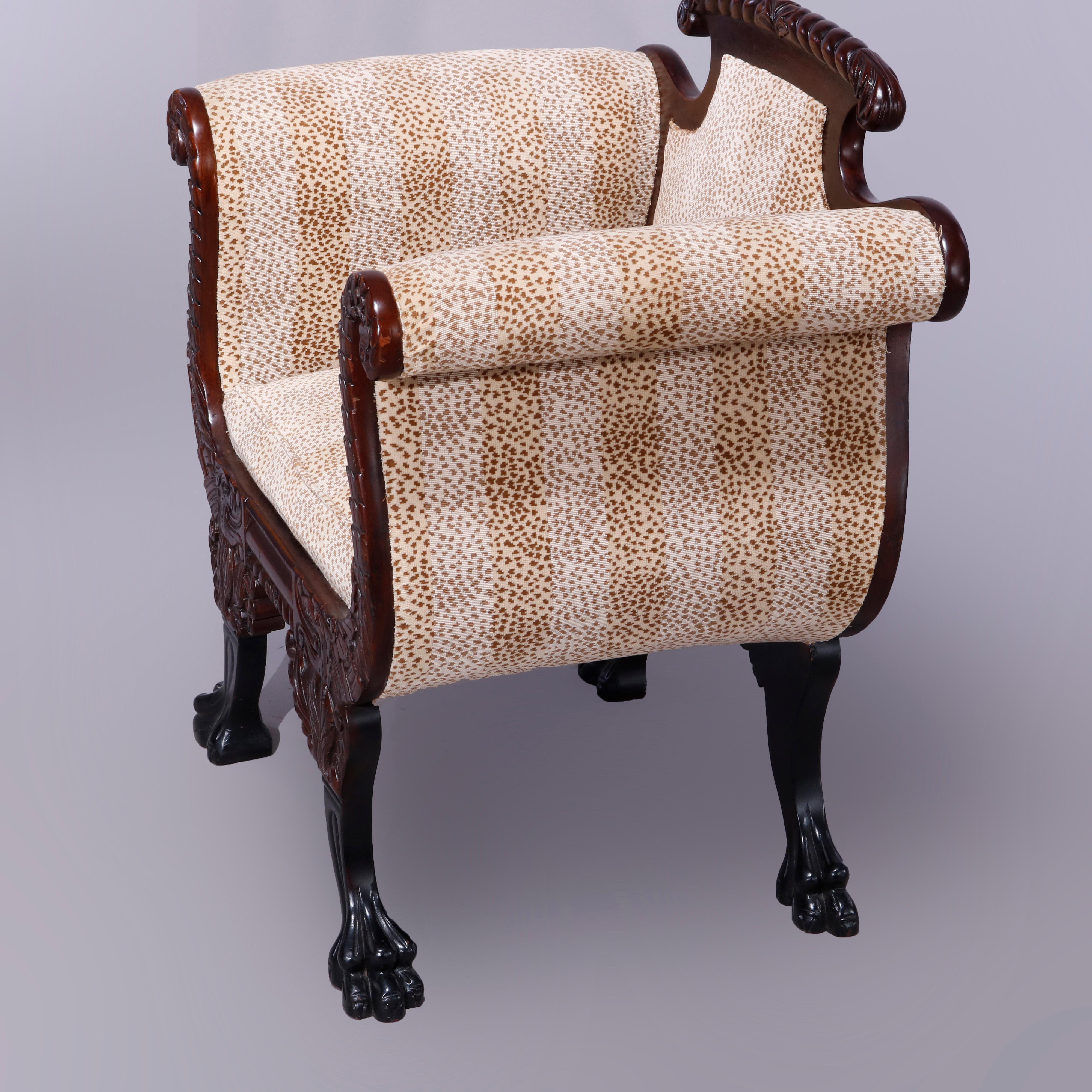 An antique American Empire neoclassical style upholstered occasional armchair offers carved mahogany frame in acanthus form with shaped back and scroll form arms raised on legs with carved paw and claw feet, upholstered in striped animal print