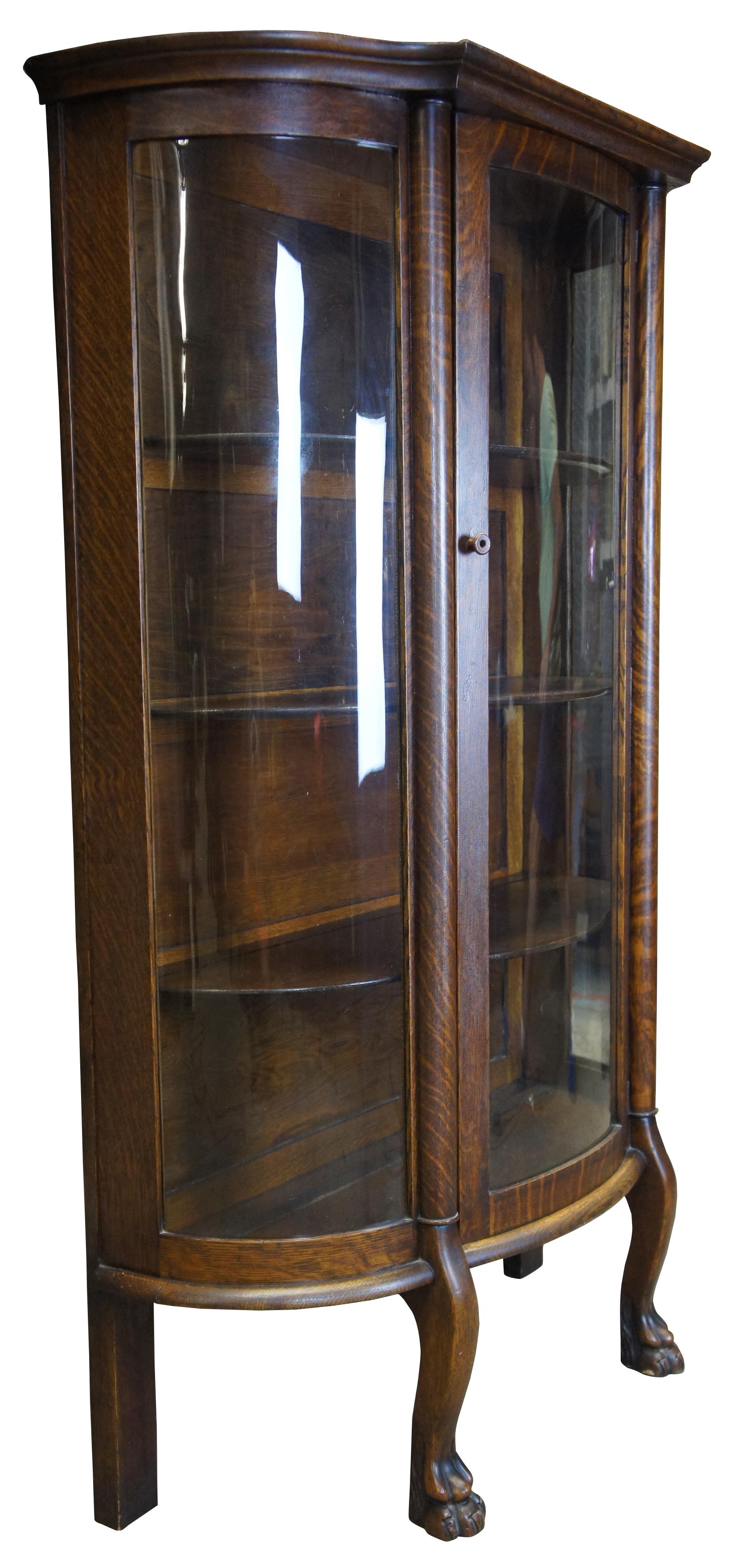 American Empire curved glass curio cabinet. Made from quartersawn oak with circular columns along the front leading to lion paw feet. Includes four shelves and plate groves.
   
Shelf clearance from bottom to top - 12.5