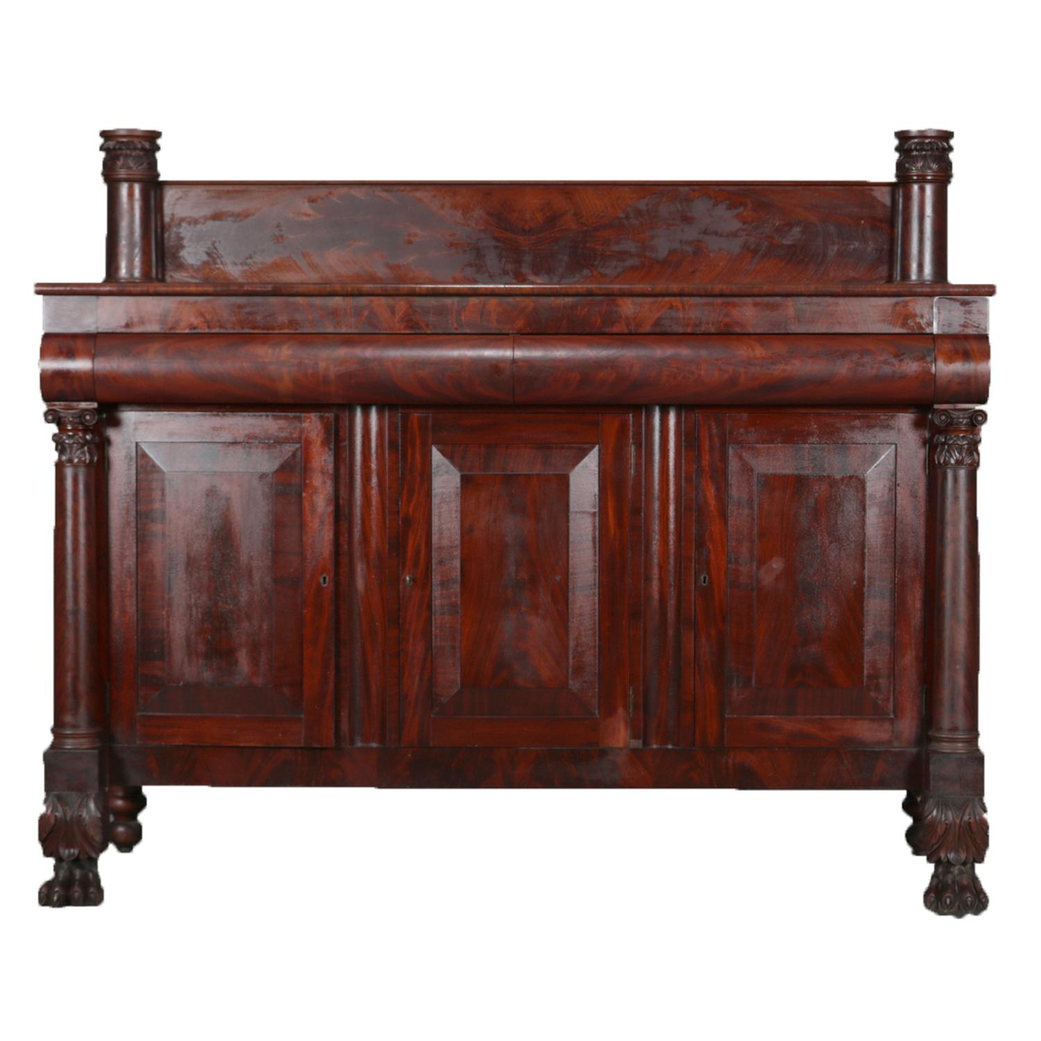 An antique Quervelle School American Empire mahogany sideboard features flame mahogany construction with backsplash flanked by full columns surmounted with deeply carved foliate capitals over case having two convex upper drawers and three lower
