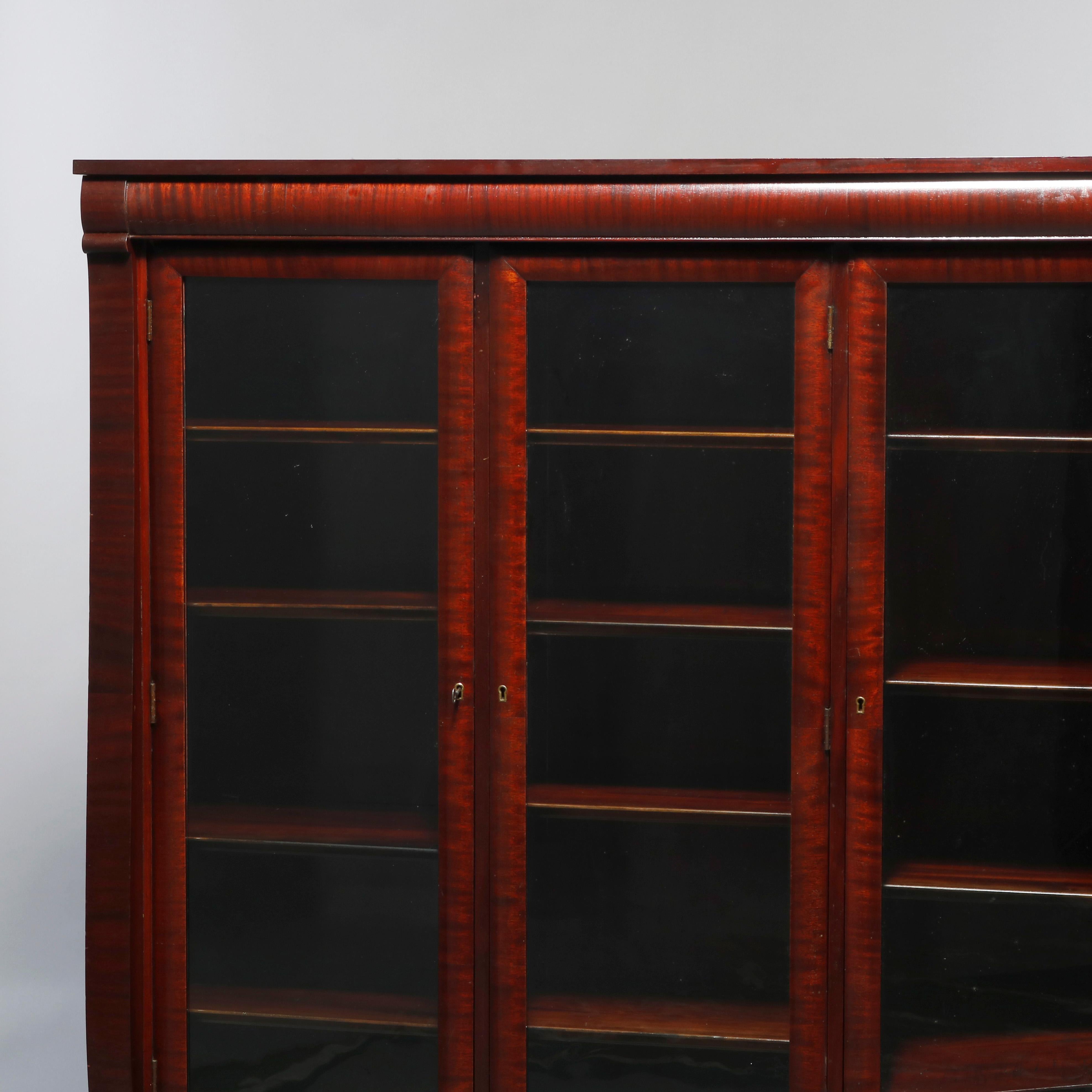 An antique American Empire style bookcase offers flame mahogany construction with three glass doors opening to shelved interior, raised on scroll form legs, c1890

Measures: 59