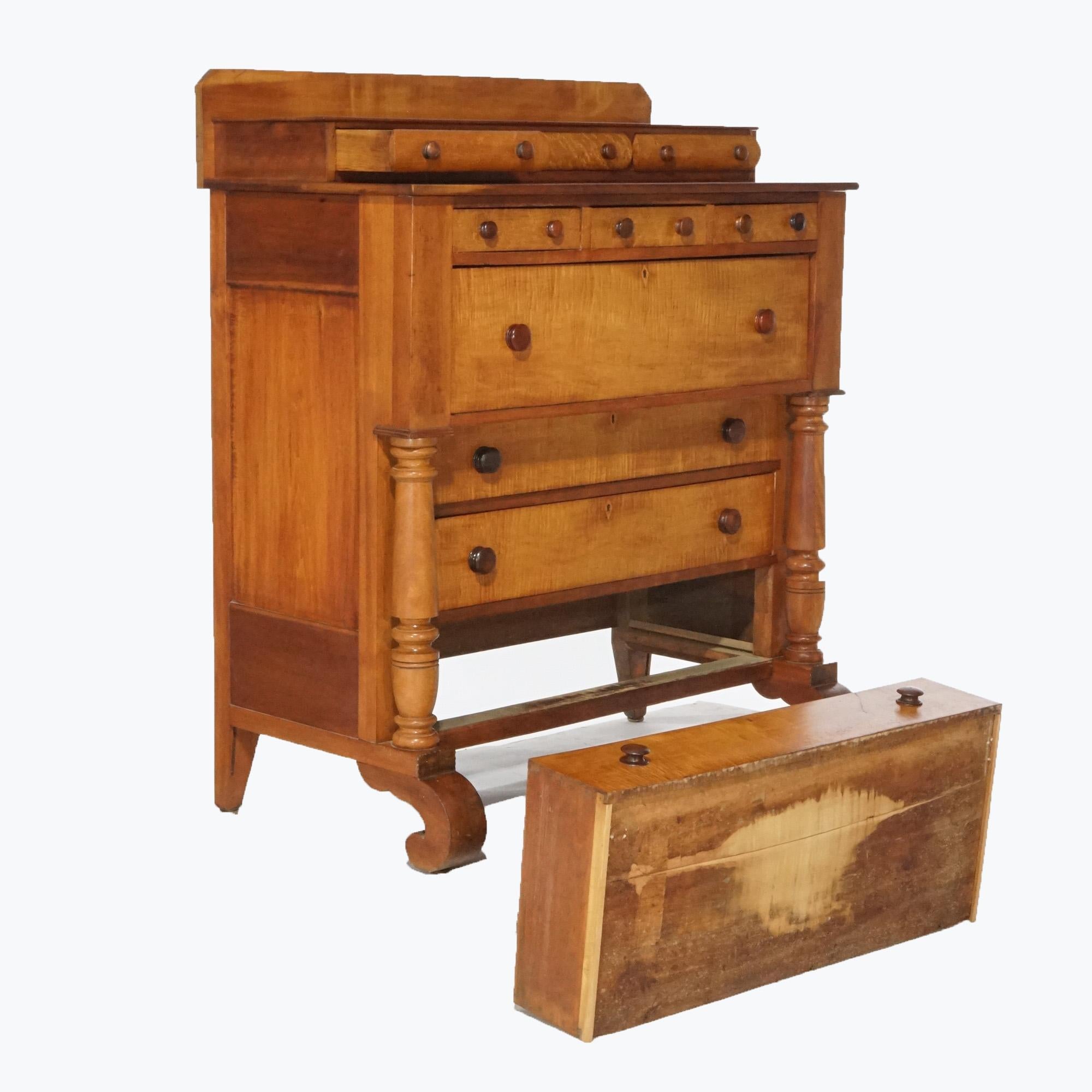An antique American Empire chest of drawers offers tiger maple and cherry construction with backsplash having convex drawers over paneled case having deep frieze drawer over lower long drawers flanked by full columns and raised on scroll form feet,
