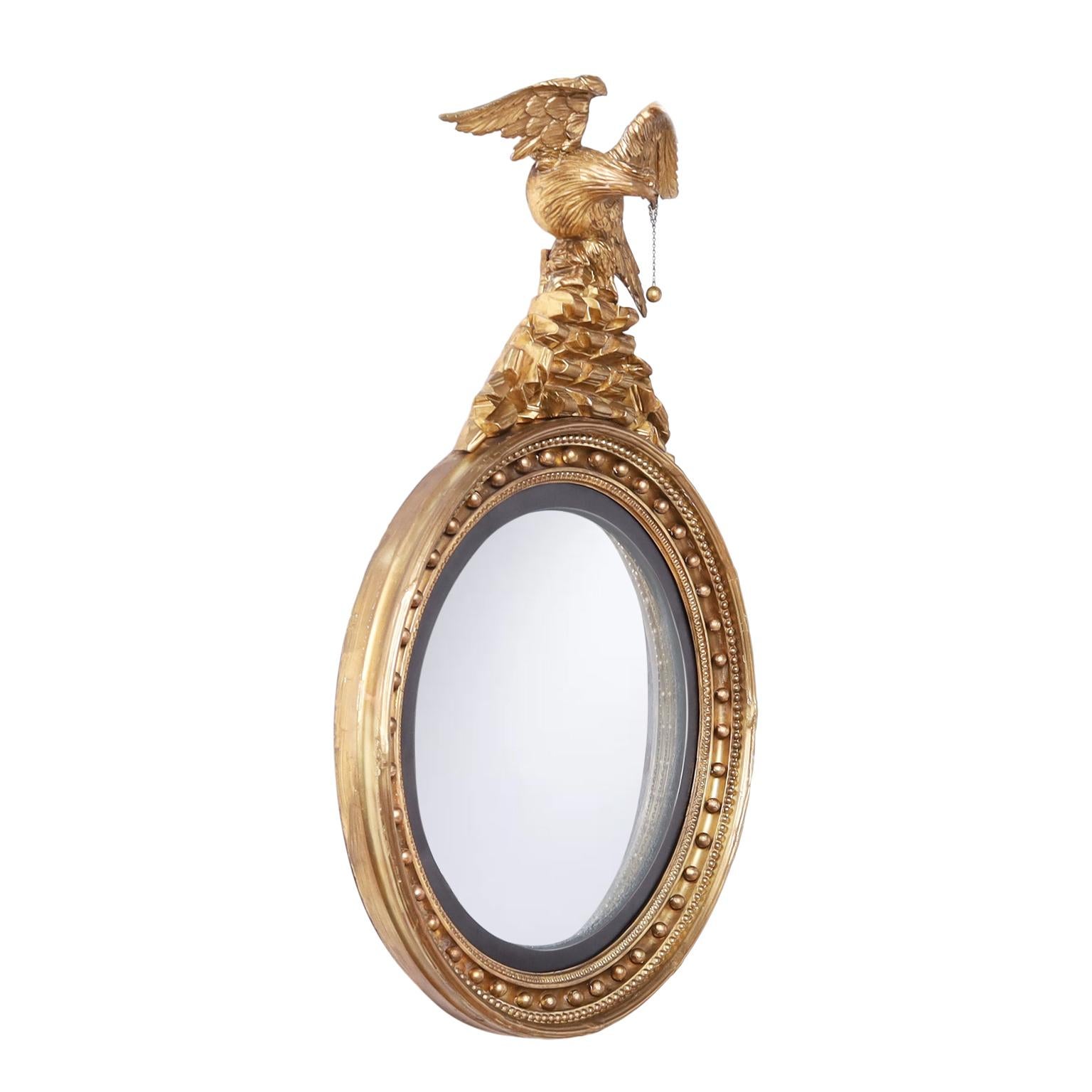 Lofty early 19th Century American federal bullseye wall mirror hand crafted in wood having a carved eagle holding a ball and chain at the top perched on a mountain over a classical round wood frame with plaster relief and wood balls around a convex