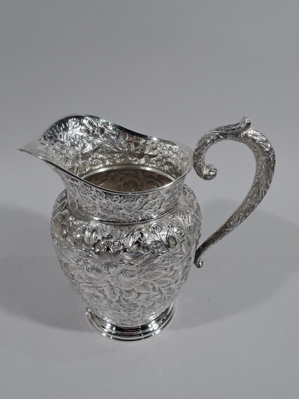 Beautiful repousse sterling silver water pitcher. Made by Manchester in Providence, circa 1910. Curved and tapering body, leaf-capped high-looping handle, and helmet mouth. Allover loose flowers on stippled ground. Plain stepped foot. Fully marked