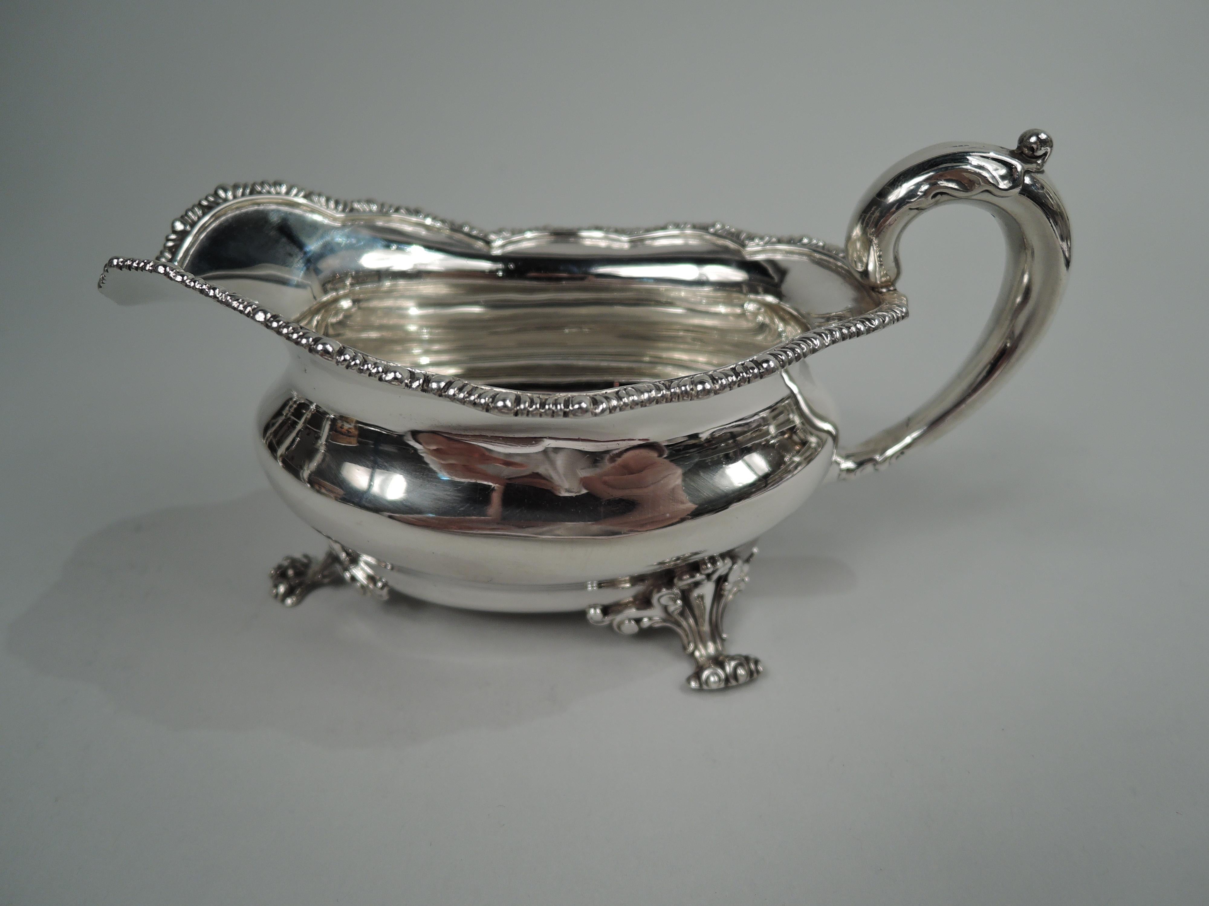 American Georgian sterling silver sauceboat, ca 1900. Retailed by Black, Starr & Frost in New York. Bellied oval bowl with leaf-capped high-looping handle and gadrooned scalloped rim; four scroll-mounted paw supports. Fully marked including