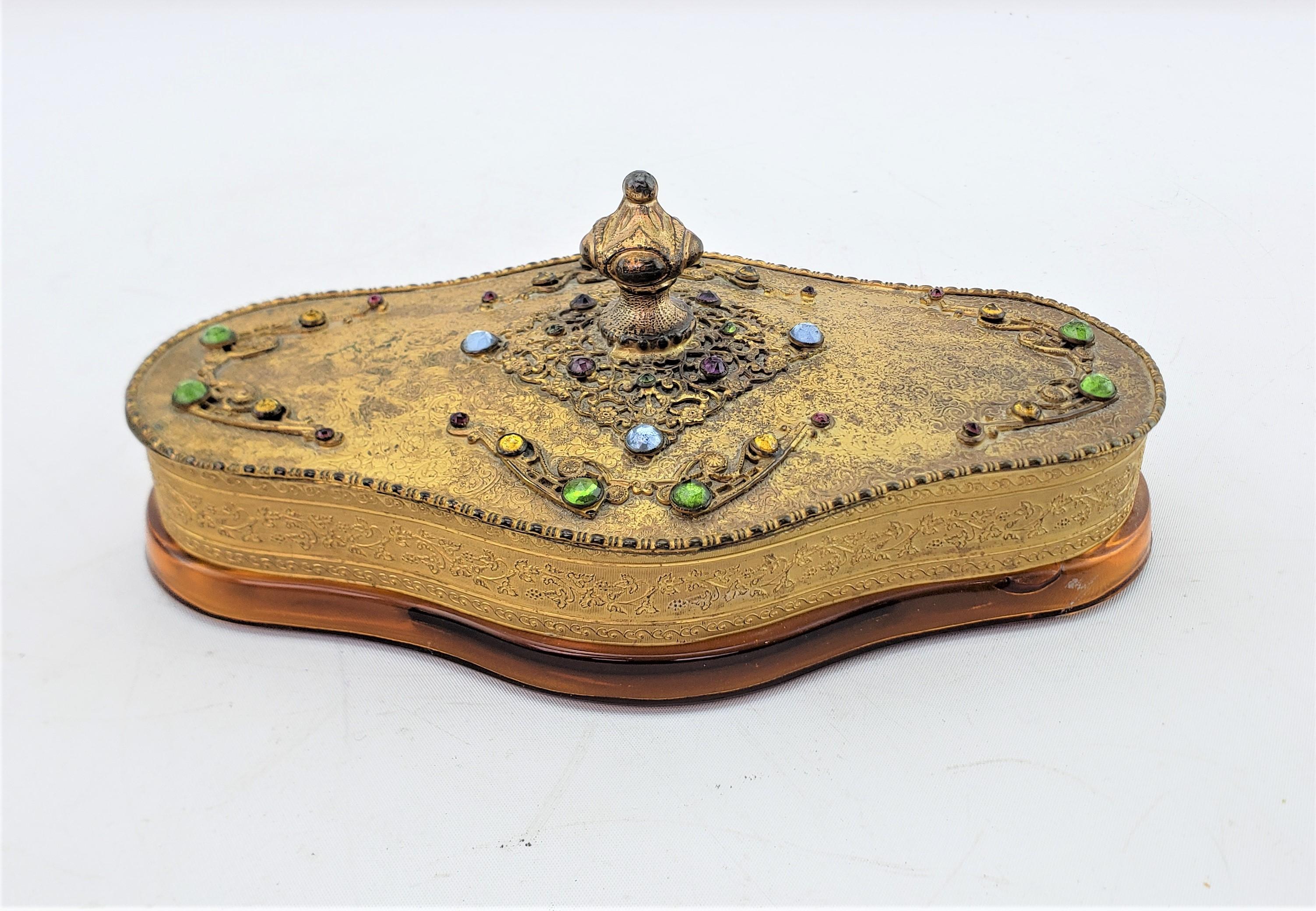 This antique decorative box was made by the Apollo Manufacturing Company of the United States in approximately 1920 in an Anglo-Indian style. The top of the box is composed of spelter with a gilt finish and inset colored glass cabachons. The bottom