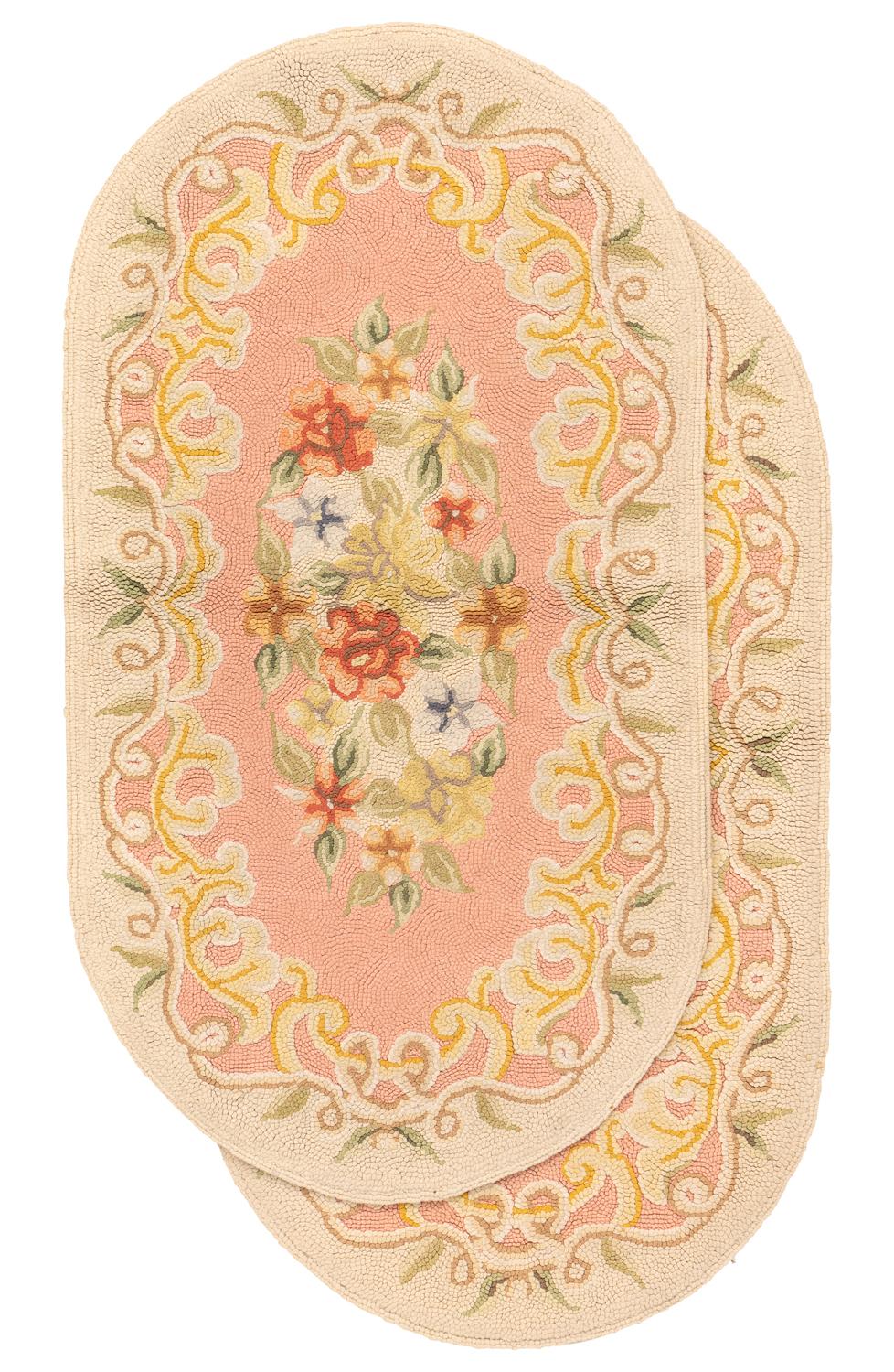 Dies ist ein Paar antiker amerikanischer Hakenteppiche, die zu Beginn des 20. Jahrhunderts um 1900 gewebt wurden und 108 x 60 cm groß sind. Diese ovalen Teppiche haben ein florales Design mit blühenden Blumen auf zartrosa Hintergrundfarbe. Die