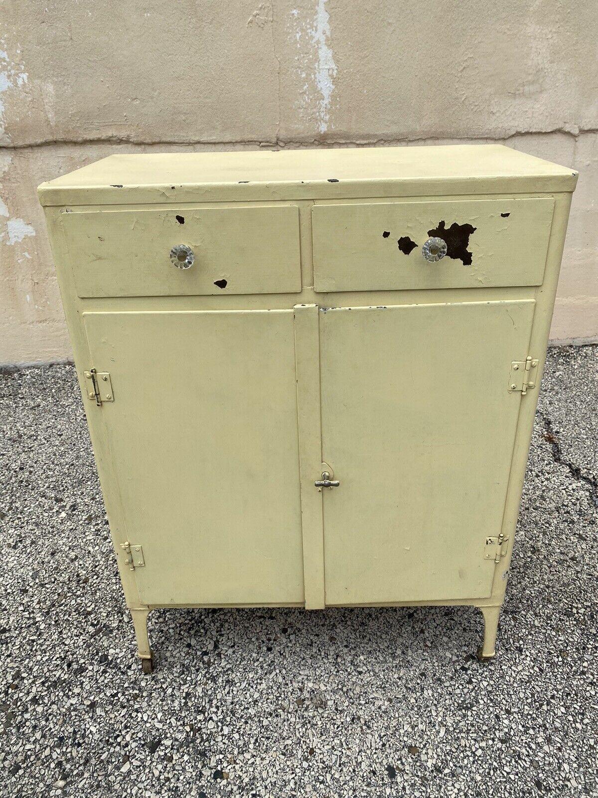 Antique American industrial steel metal yellow painted storage cabinet dresser. Item features steel metal frame, glass knob drawer pulls, 2 swing doors, 2 drawers, 1 shelf, rolling casters, distressed yellow painted finish, quality American