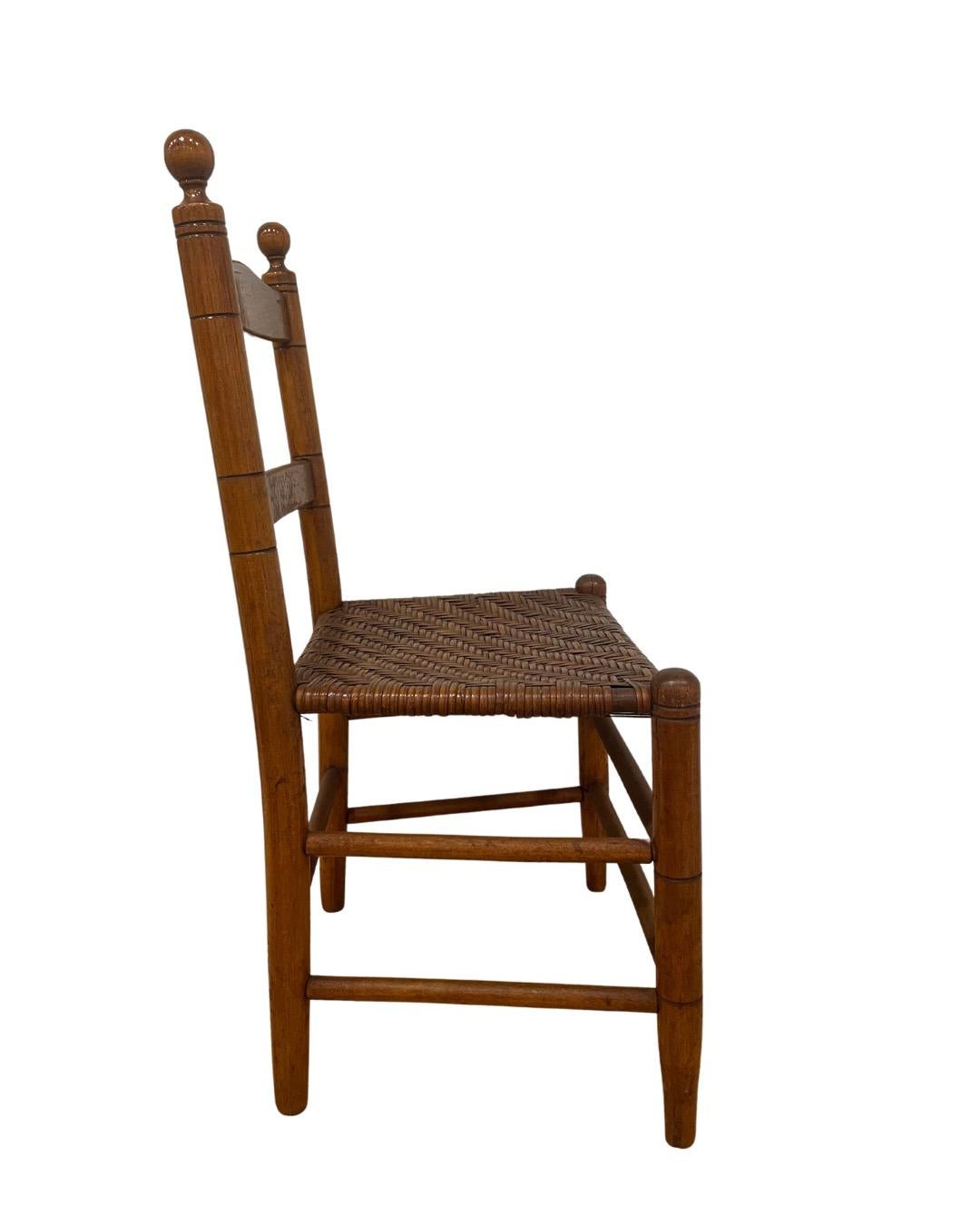 Wooden child's chair attributed to F.A. Sinclair of Mottville, NY. Estimated to be 19th century. Medium brown finish on chair and seat. 

Features include a ladder-back design, ball finials, and tapered legs. Woven splint seat in herringbone