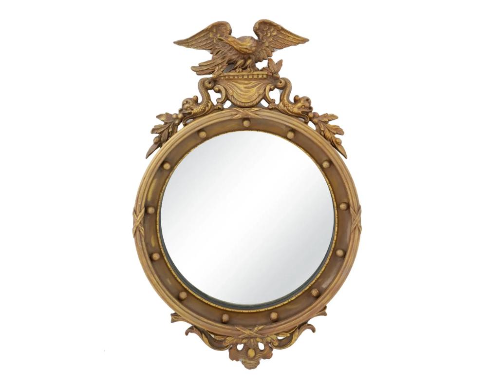 An antique American mirror features a beautifully crafted round mirror framed in ornate detailing. Circa the 19th century. The mirror is encased in a decorative gilt frame embellished with an elaborate motif that includes a majestic eagle perched at