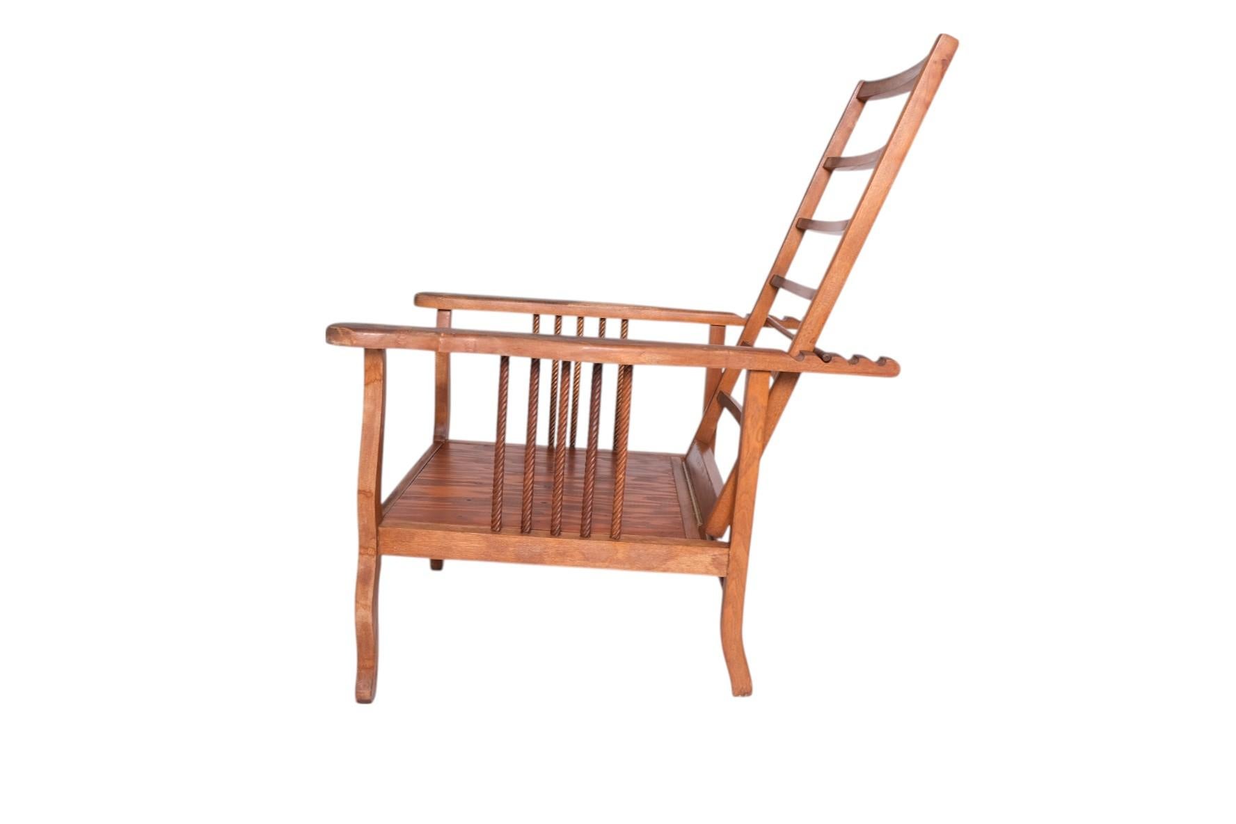 An Early 1900's American Morris chair frame, featuring a tall ladder-back design with adjustable reclining mechanism, sculpted arms, and turned rope-twist spindles along the sides. Rooted in the Arts & Crafts movement yet rendered with a rustic,