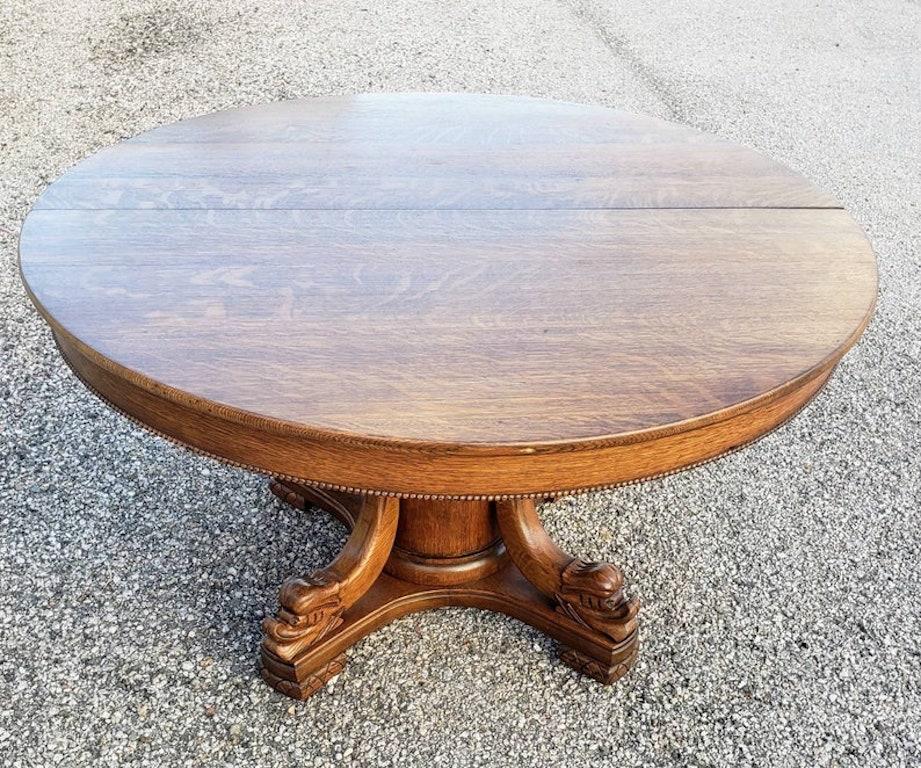 An antique turn of the century American oak extension split-pedestal dining table. Circa 1900. Having a round top over a beaded skirt, rising on a cylindrical pedestal, four stylized dolphins on the raised base, not accompanied by