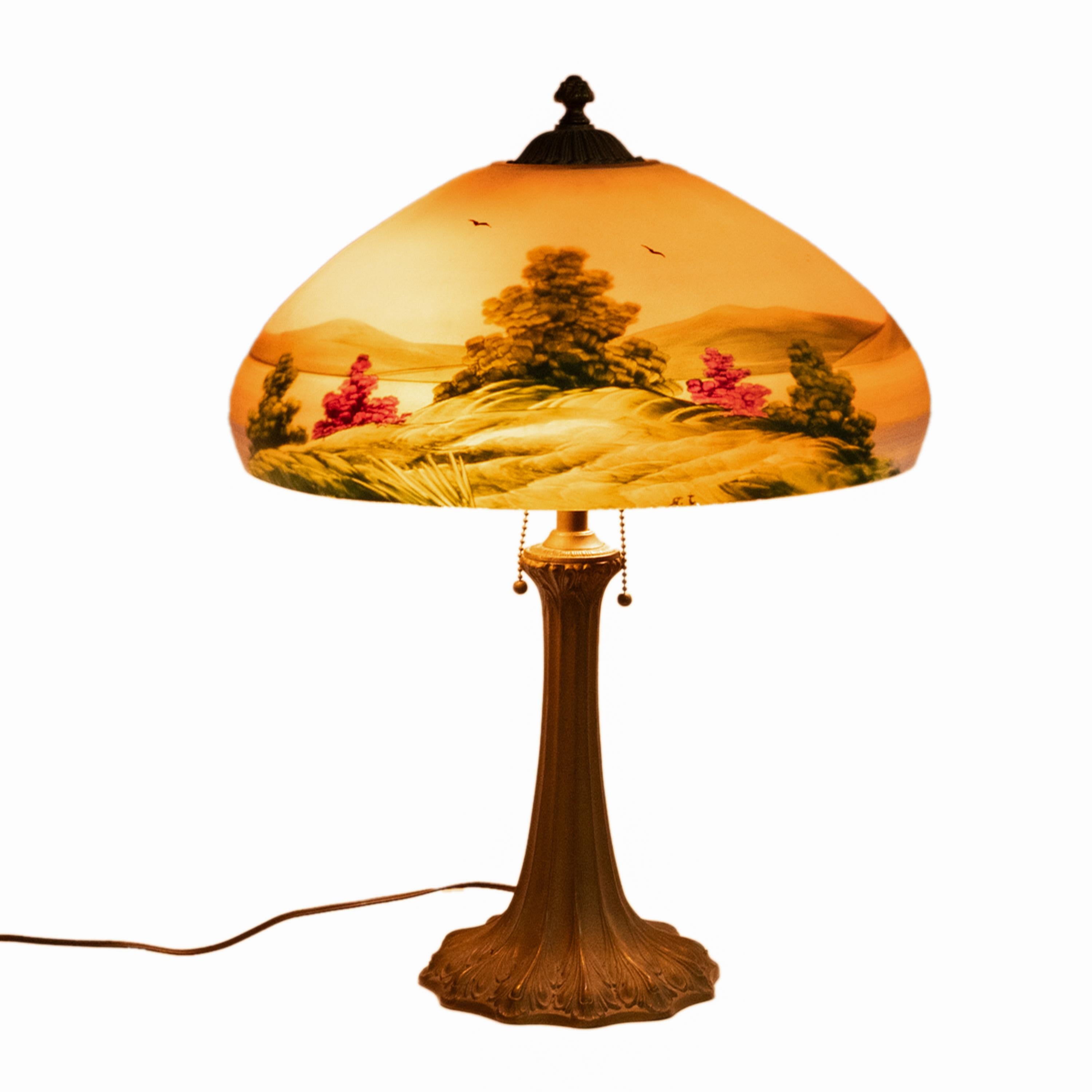 A good antique American Arts & Crafts reverse painted table/parlor lamp, by the Pittsburgh Lamp & Glass Co., circa 1910.
This very attractive antique lamp having a dome shaped shade upon a gilded bronze base. The shade is reverse painted with a