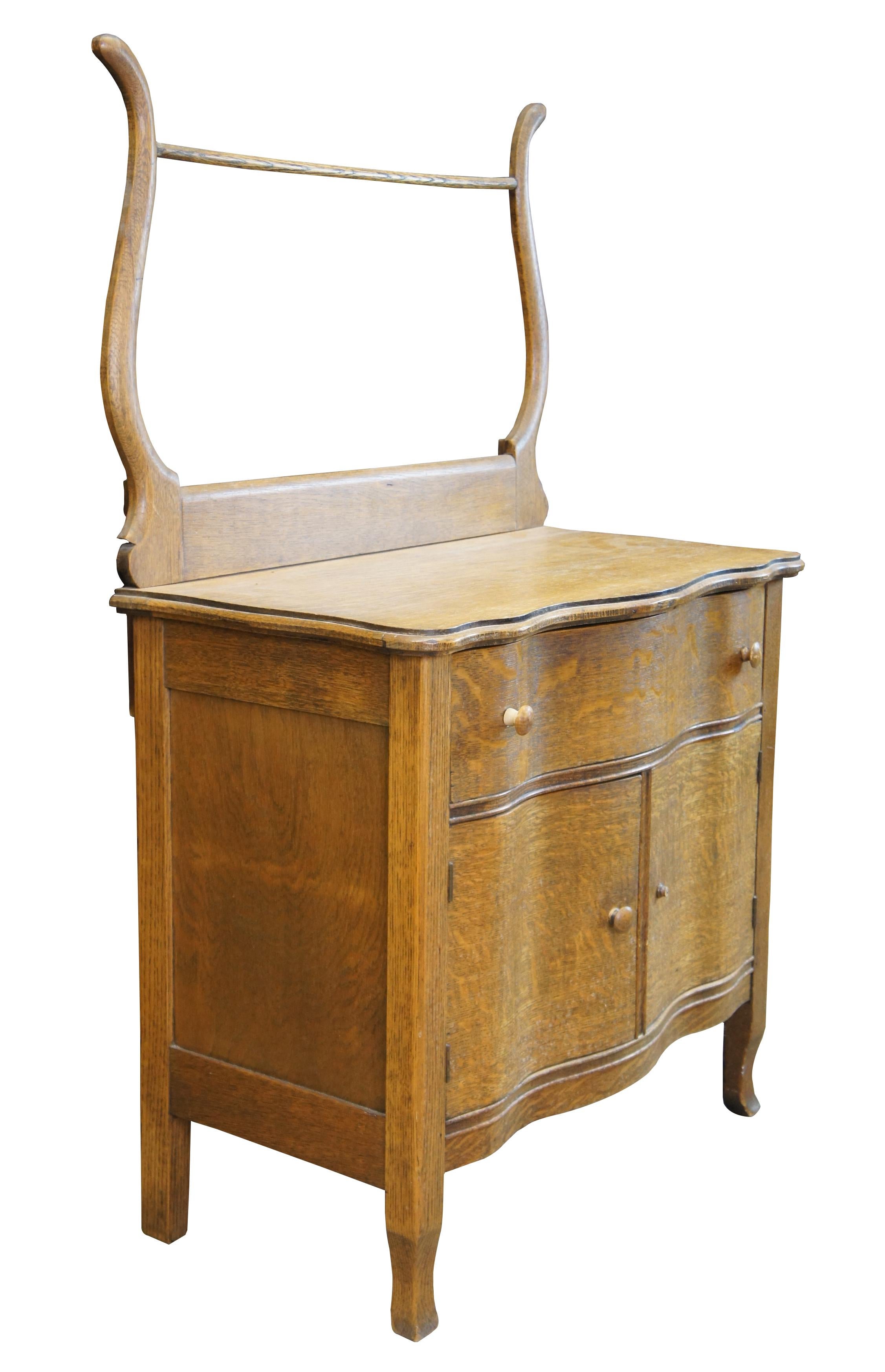 Antique early American wash stand, dry sink or commode. Made of quartersawn oak featuring serpentine form with lower cabinet, one drawer and upper towel bar.

Surface Height - 29