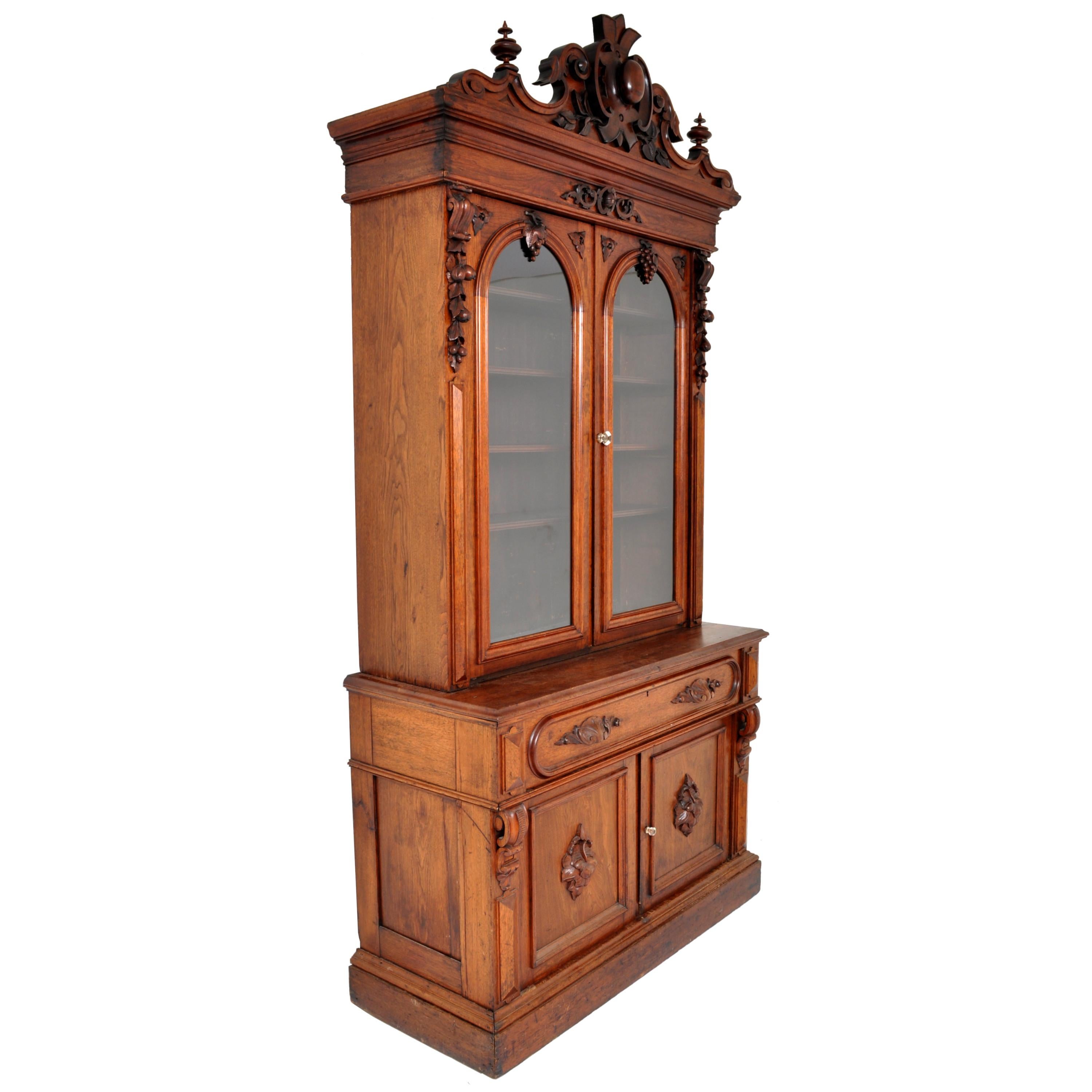A very grand antique American Renaissance Revival carved bookcase secretary, circa 1870. The bookcase in two parts, the top bookcase having an ornately carved crown with floral and architectural detail and flanked by twin turned finials. Below are