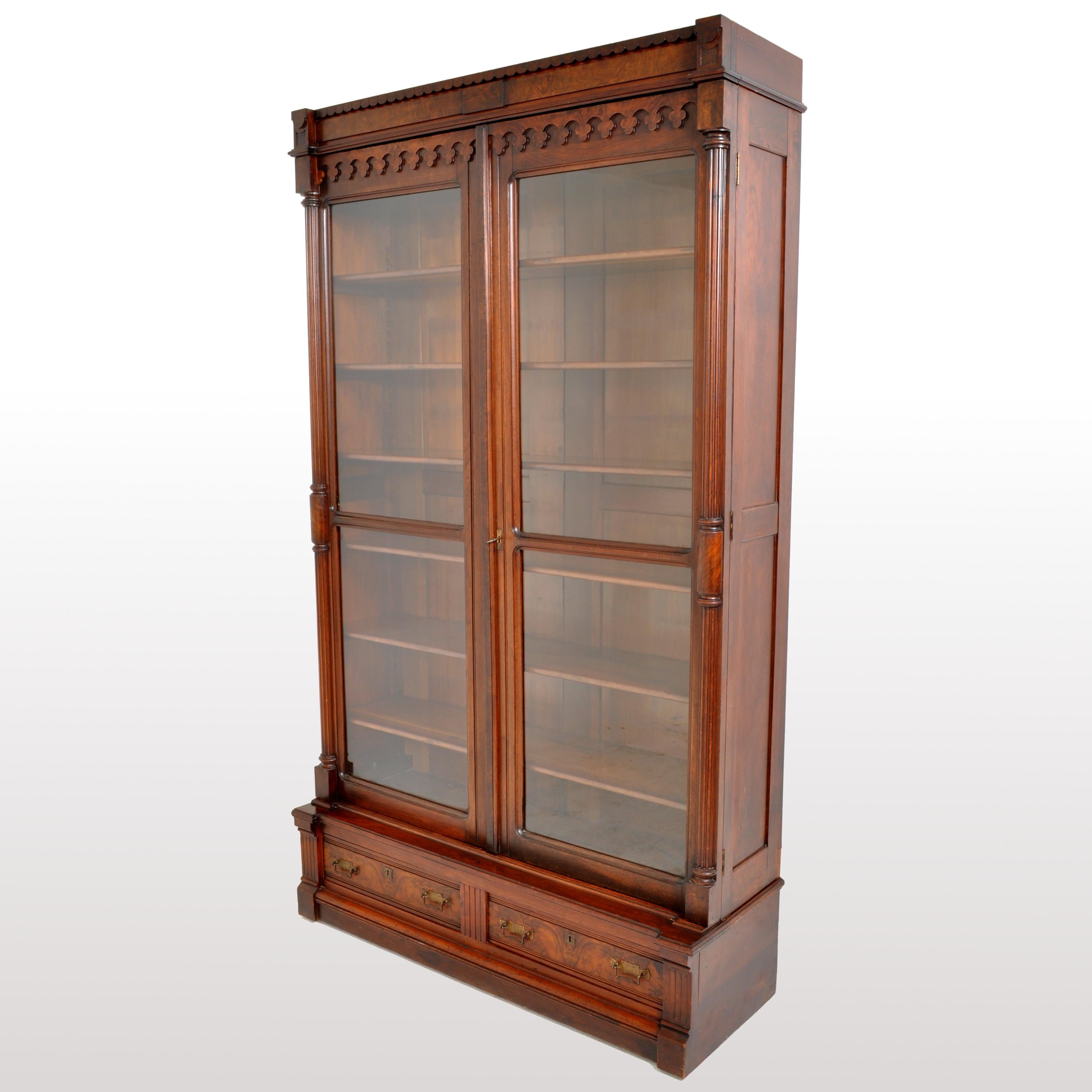 A fine antique American Eastlake/Renaissance Revival, tall, walnut and burl-walnut bookcase, circa 1875. The bookcase having a carved crown with a carved gallery below, the twin doors each having a full length ribbed and turned column. The doors