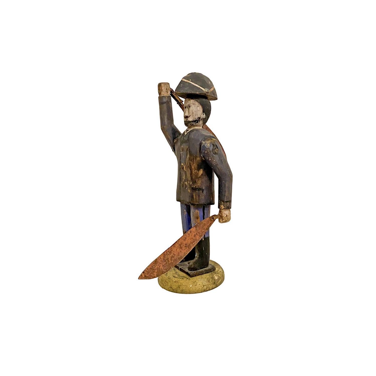 Carved and painted Pine with rotating sheet iron swords, with black hair, mustache and beard, bicorn hat, blue jacket with tacks for buttons, black boots mounted on a yellow circular base, original surface. American, Measure: 15” high, c. 1900