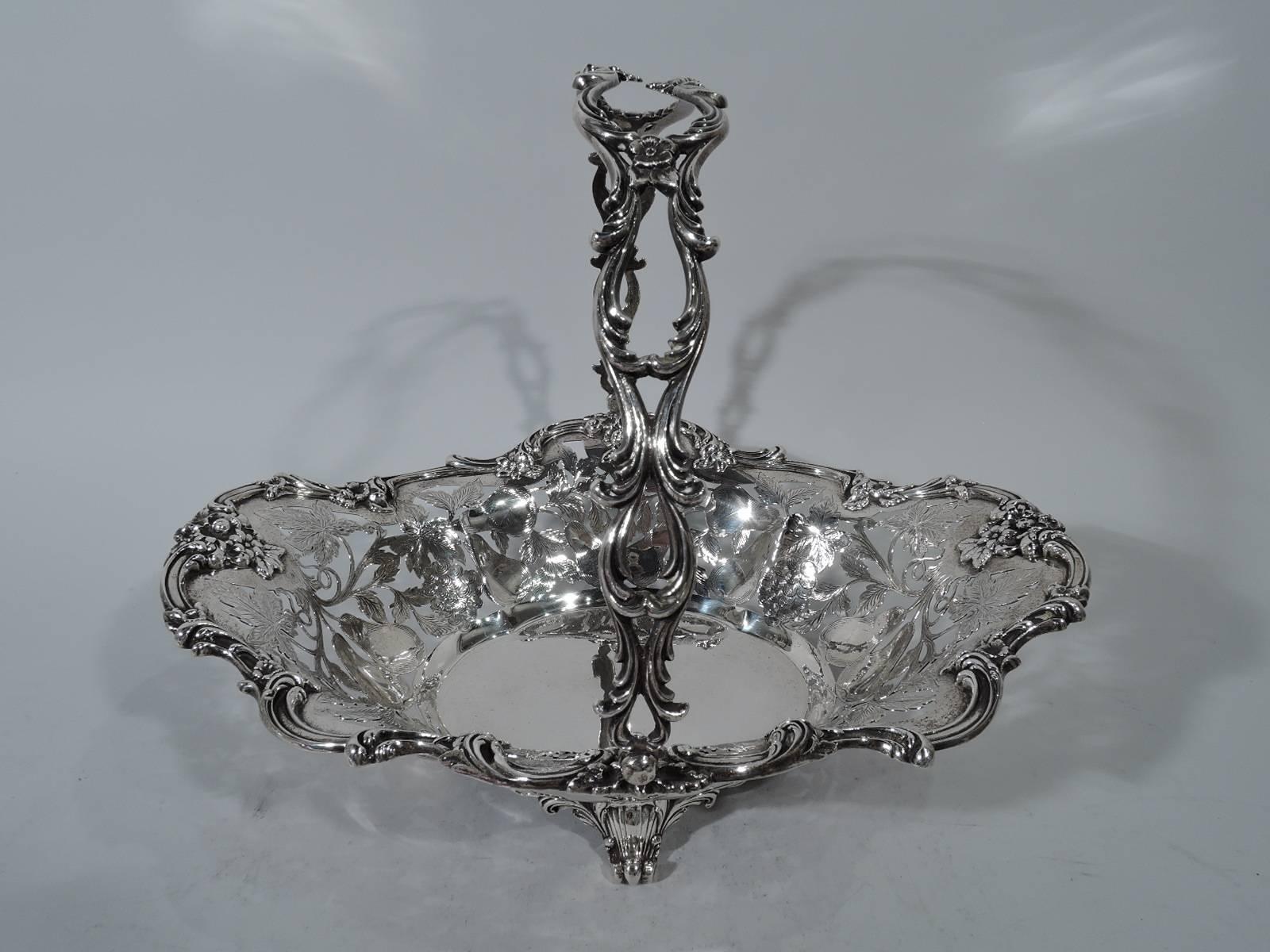 Victorian sterling silver basket. Made by Roger Williams (later part of Gorham) in Providence. Solid quatrefoil well. Sides tapering with open fruits and leaves engraved on interior. Scrolls and flowers applied to rim. Open swing handle with same.