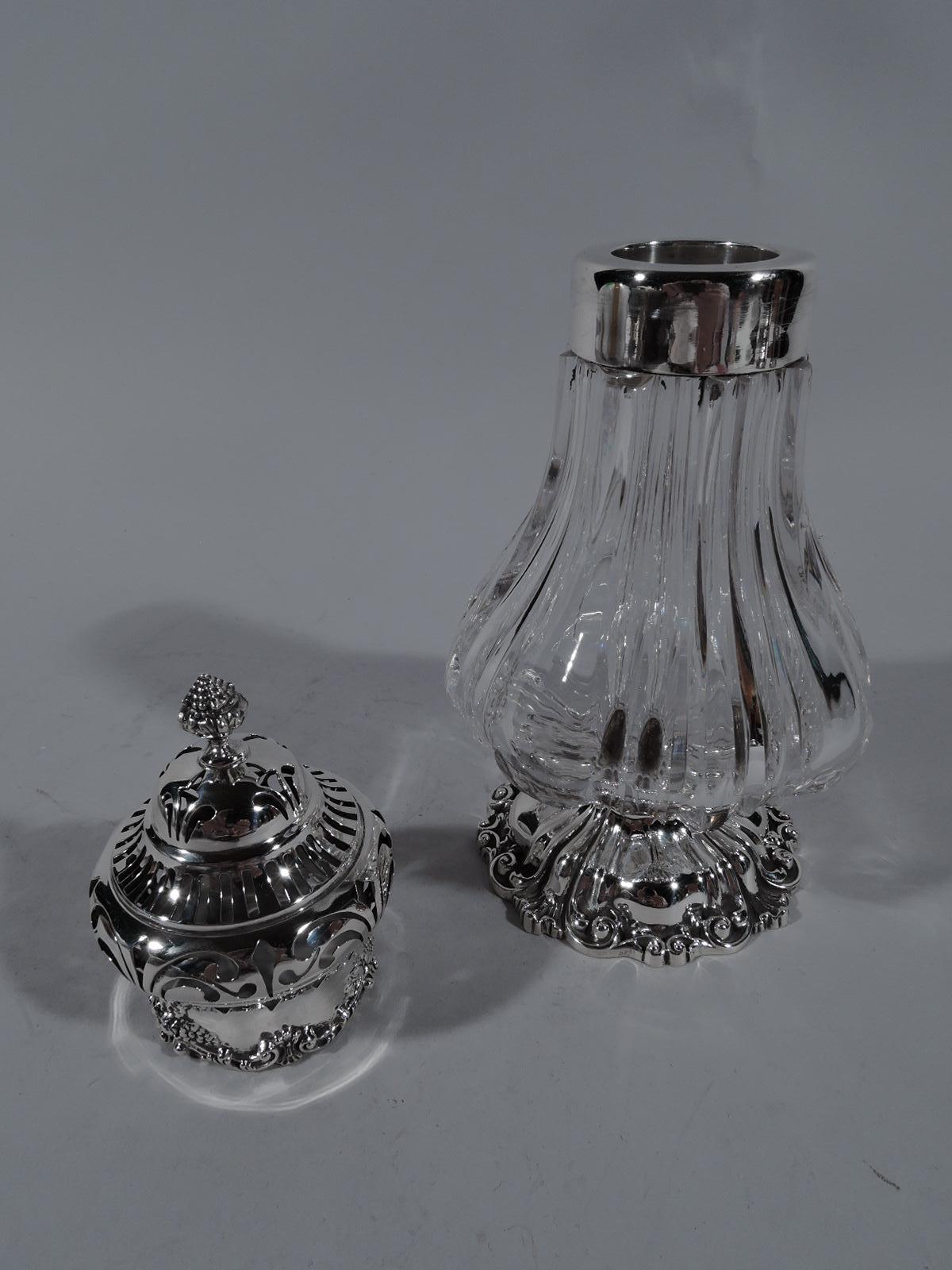 Turn of the century crystal sugar Shaker with sterling silver mounts. Made by Durgin in concord. Fluted baluster body on raised and scrolled foot. Domed cover with ornamental piercing, berry finial, and scroll and flower border applied at rim. Fully