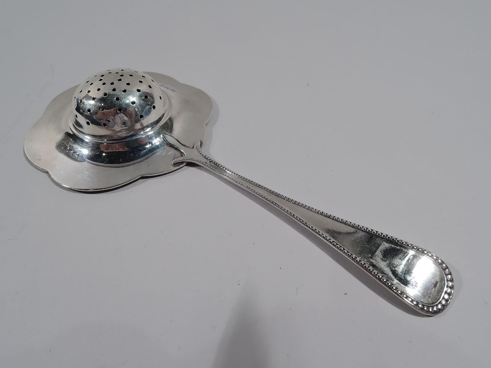 American sterling silver tea strainer, circa 1920. Round and pierced bowl and beaded and scalloped petal rim. A functional flower head mounted to a tapering and beaded handle. Marked “Sterling” and numbered “1062”. Weight: 1.3 troy ounces.