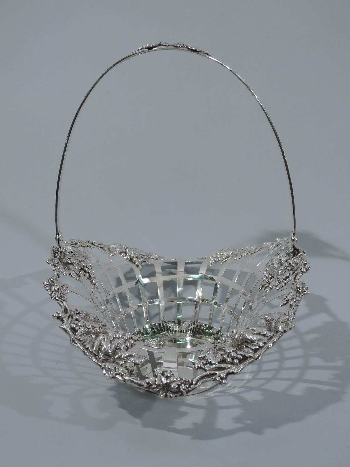 Turn-of-the-century American sterling silver basket. Solid and oval well. Sides open trellis with flared ends. Irregular vine rim with grape bunches applied to interior. Reeded and tapering swing handle with leaves applied to open center. Fully