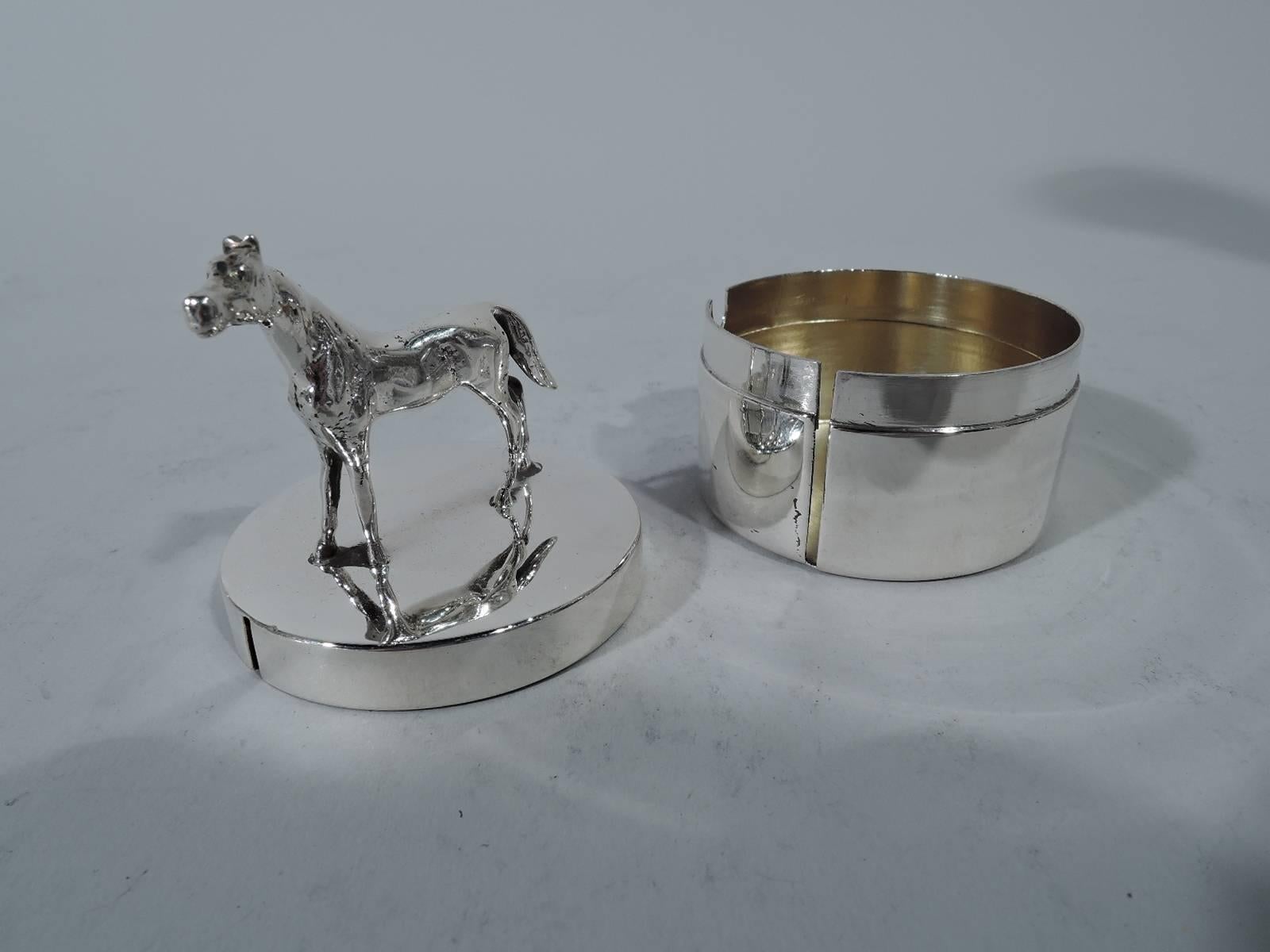 American sterling silver postage stamp box, circa 1920. Round with straight sides. Cover flat with cast finial in form of horse. Vertical slit for threading roll. Hallmarked Herbst & Wassall, a Newark maker active in the first decades of the 20th