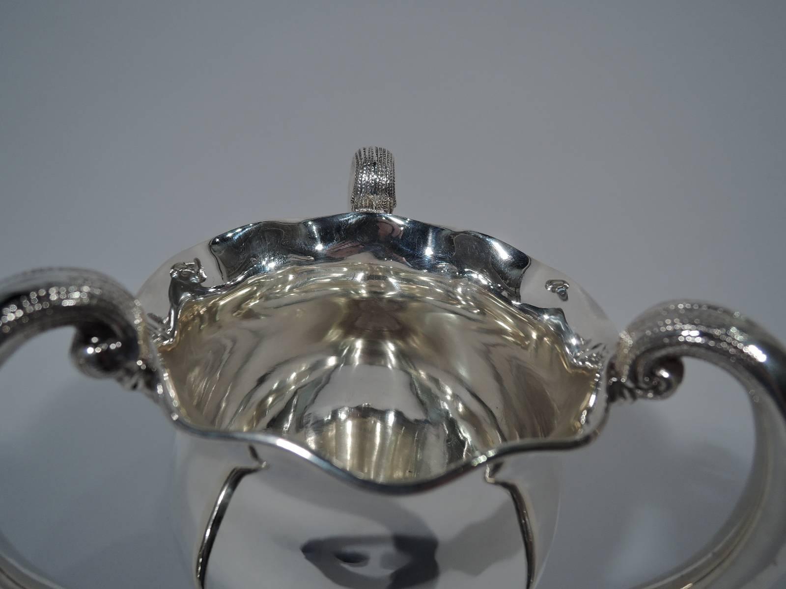 Sterling silver trophy cup. Made by Black, Starr and Frost in New York, circa 1900. Baluster bowl with ruffled rim, three high-looping and tapering handles with stippled “cap”, and raised star foot with applied scrolls and fleur-de-lys. Hallmark