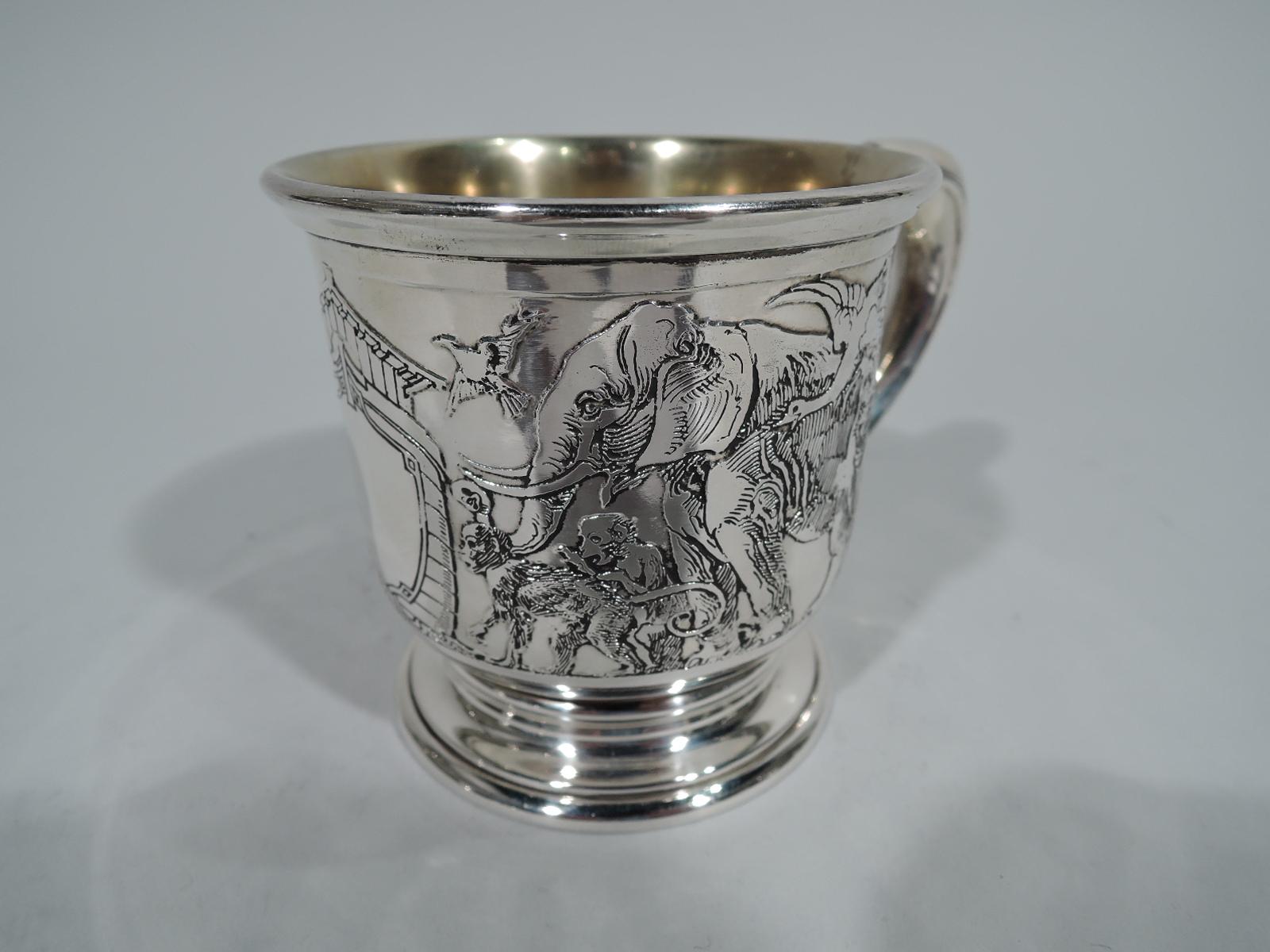 Edwardian sterling silver baby cup with Noah’s Ark theme. Made by Kerr in Newark, circa 1900. Flared rim, scrolled bracket handle, and stepped foot. The Ark is flanked by foxes, cats, elephants, and lions. A dense and lively frieze – less an orderly