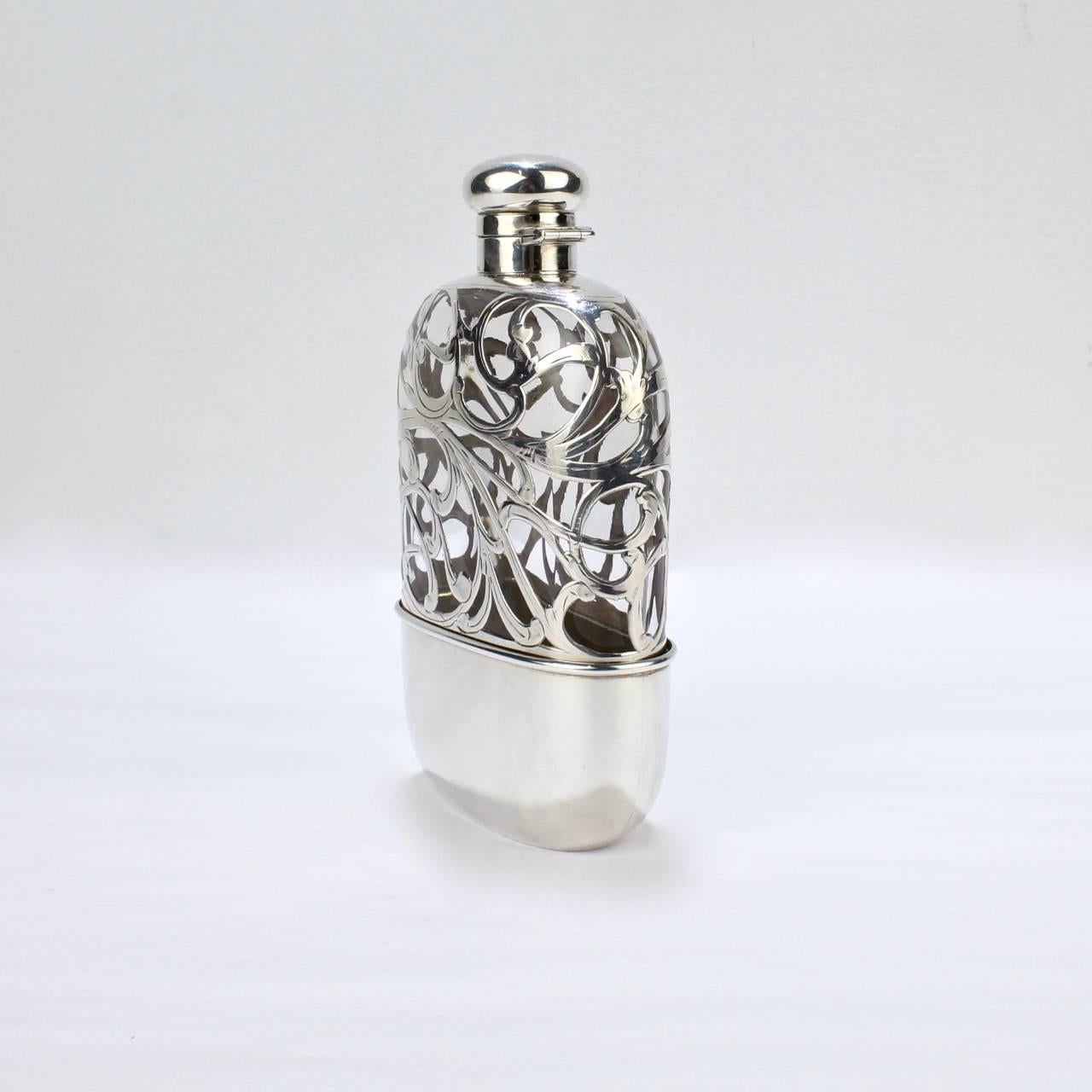 A terrific antique American hip or pocket flask.

Constructed of glass and sterling silver with a twist cap, Art Nouveau sterling silver overlay to the body, and a gold-washed removable drinking cup.

The interior of the cap's hinge is stamped